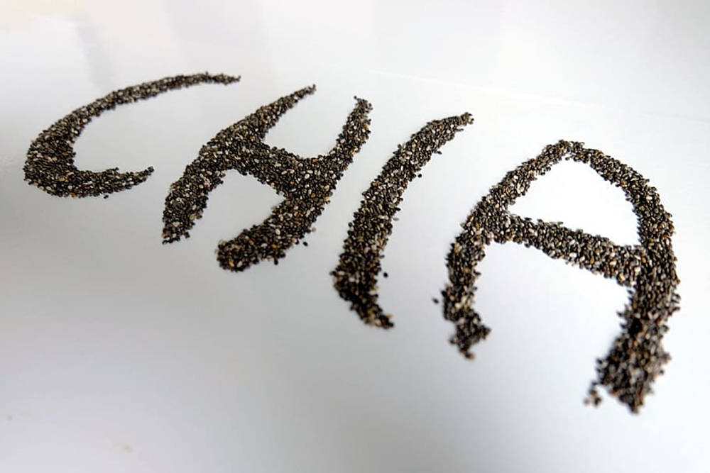 奇亞籽拼寫「Chia」字樣 壁紙 — 喺明亮白色表面上用深色斑點奇亞籽拼出嘅「CHIA」呢個字。