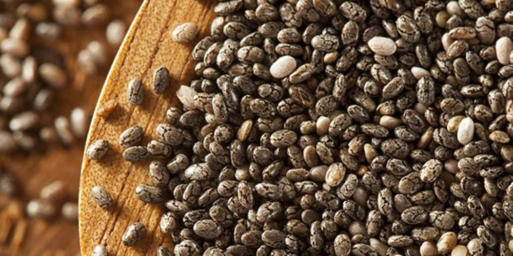 奇亞籽特寫 壁紙 — 特寫鏡頭顯示深色斑點奇亞籽從木勺灑落到質樸的木質表面上。