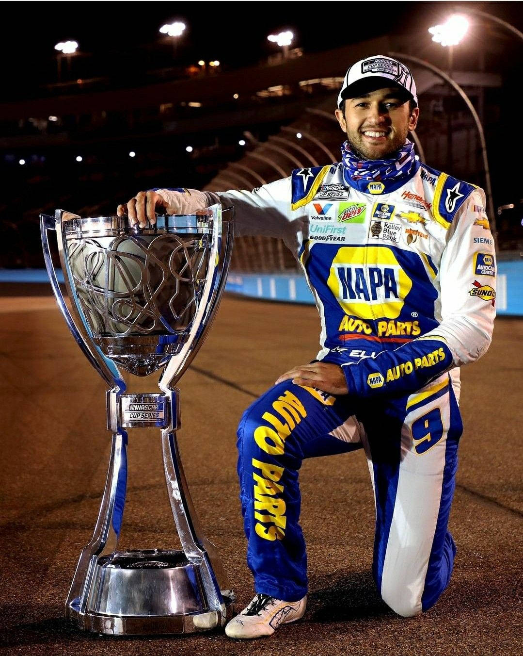 NASCAR車手在夜間的賽道上跪在其冠軍獎盃旁。