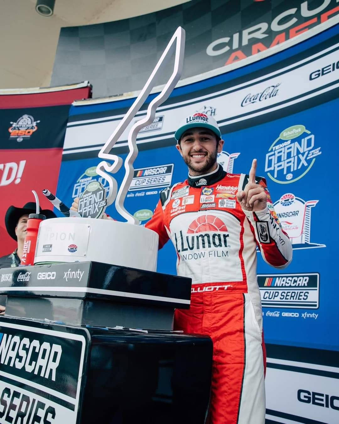 NASCAR車手在德州大獎賽頒獎台上手持獎盃慶祝勝利。