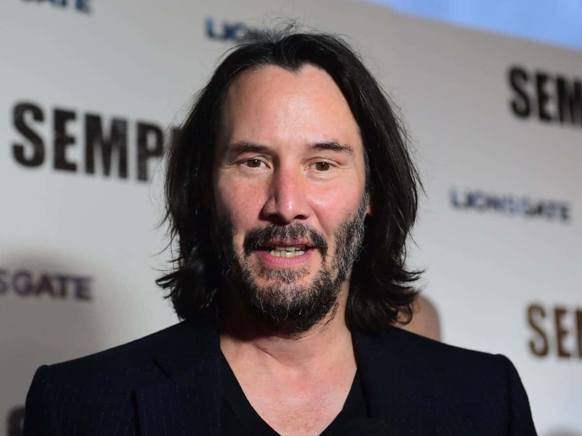 Keanu Reeves 桌布 壁紙 — 奇洛·李維斯在獅門影業活動中對著鏡頭微笑，背景顯示「SEMPER」字樣。