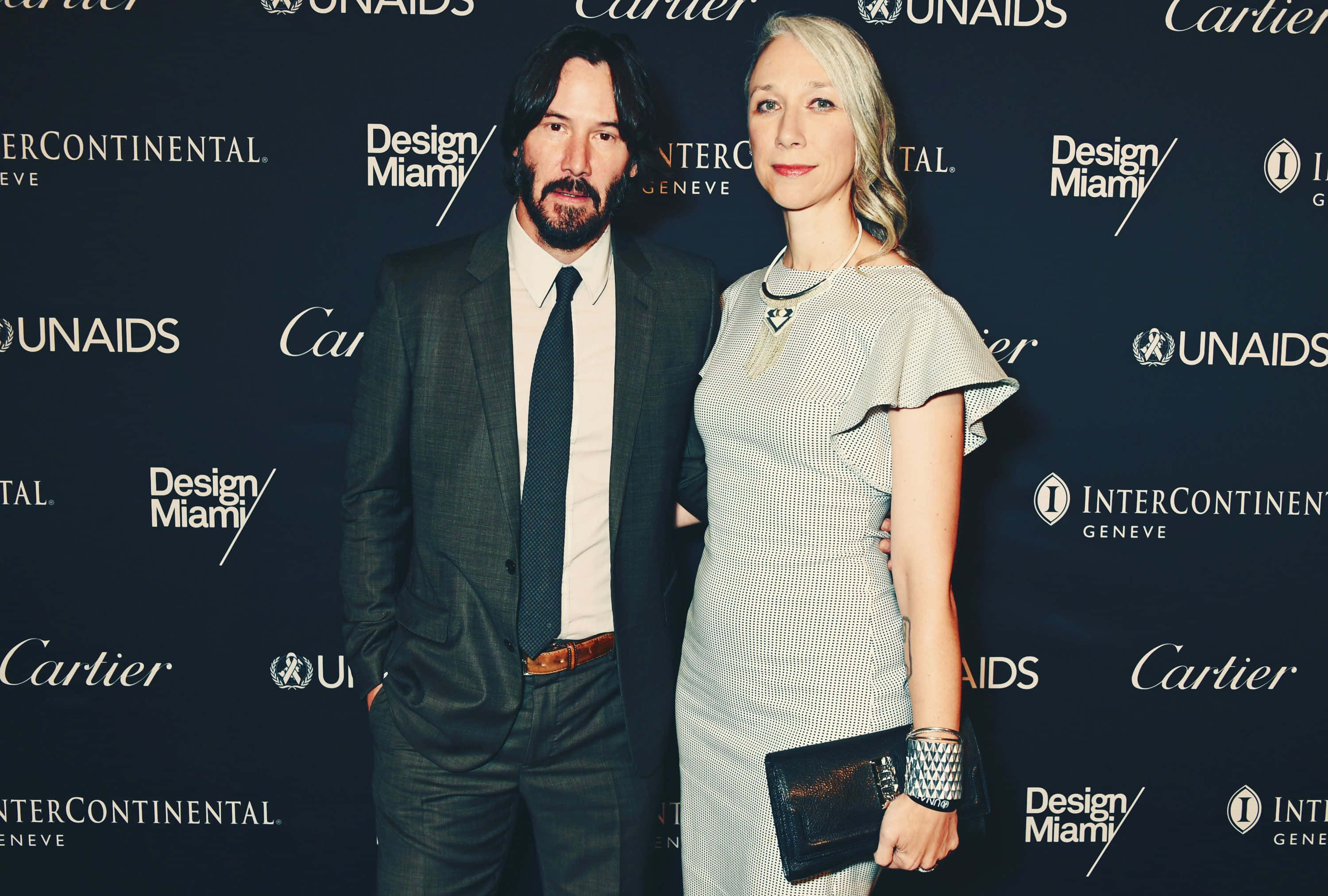 Keanu Reeves 桌布 壁紙 — 奇洛·李維斯與一位女士在一個豪華活動中，於印有卡地亞和Design Miami標誌的品牌背景前優雅地擺姿勢。