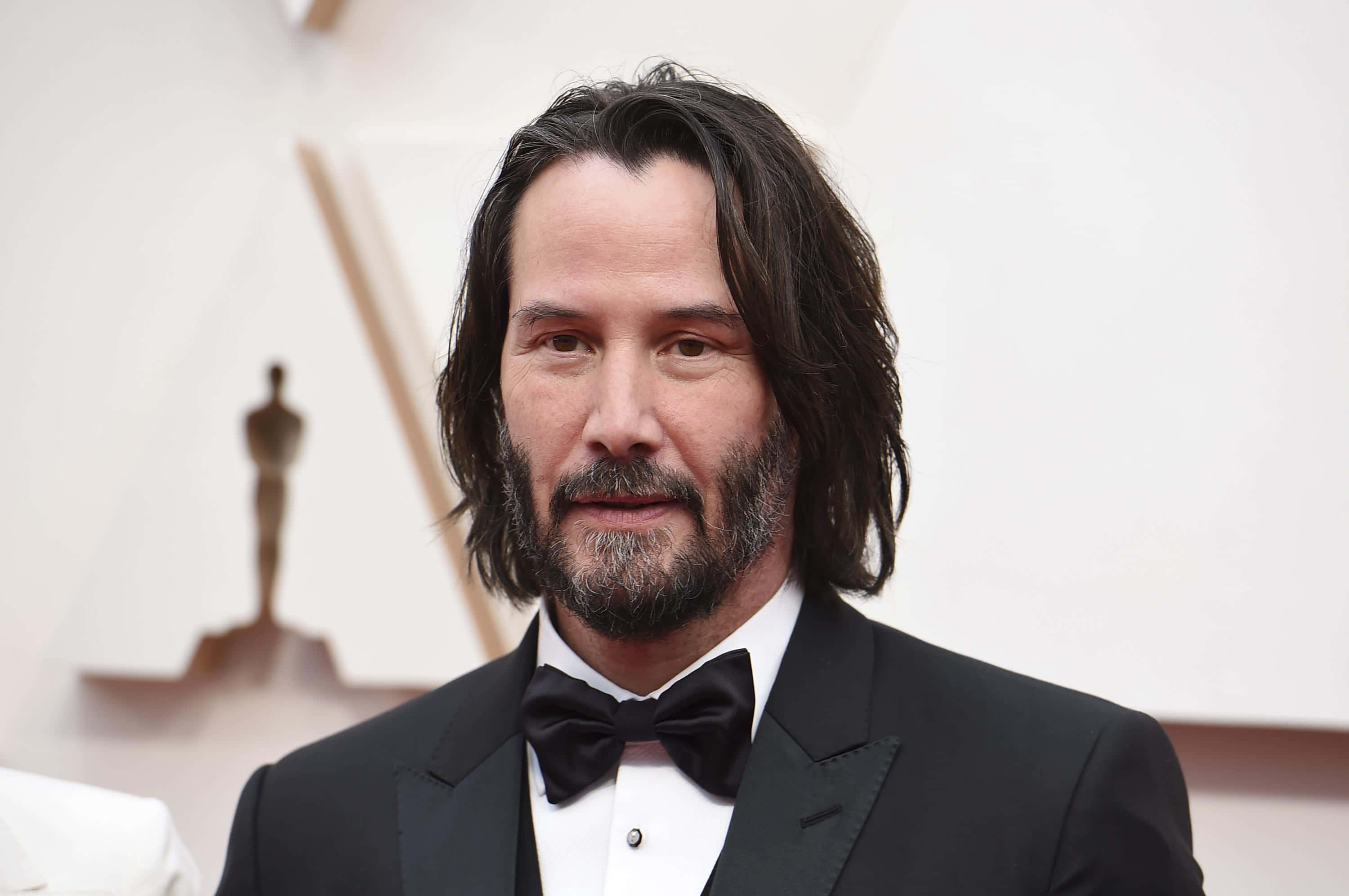 Keanu Reeves 桌布 壁紙 — 奇洛·李維斯身穿黑色禮服配蝴蝶結，在頒獎典禮上自信地站立，背景有奧斯卡獎座。