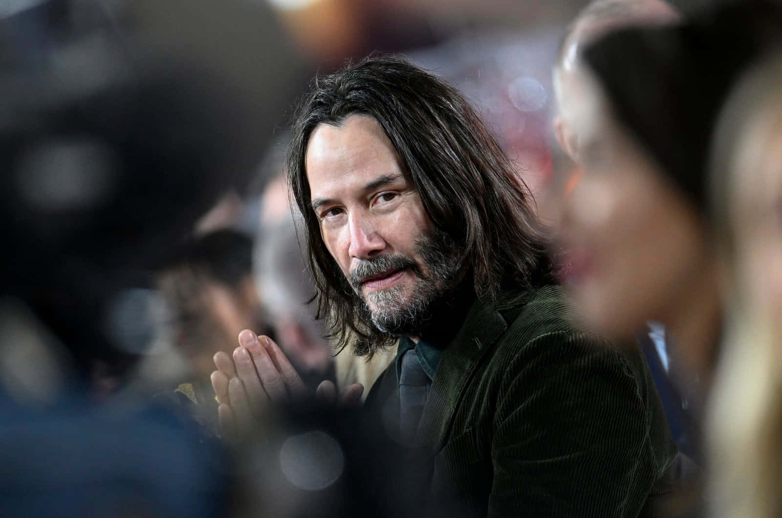 Keanu Reeves 桌布 壁紙 — 奇洛李維斯留著長黑髮和鬍鬚，在模糊的人群中拍手參加活動。