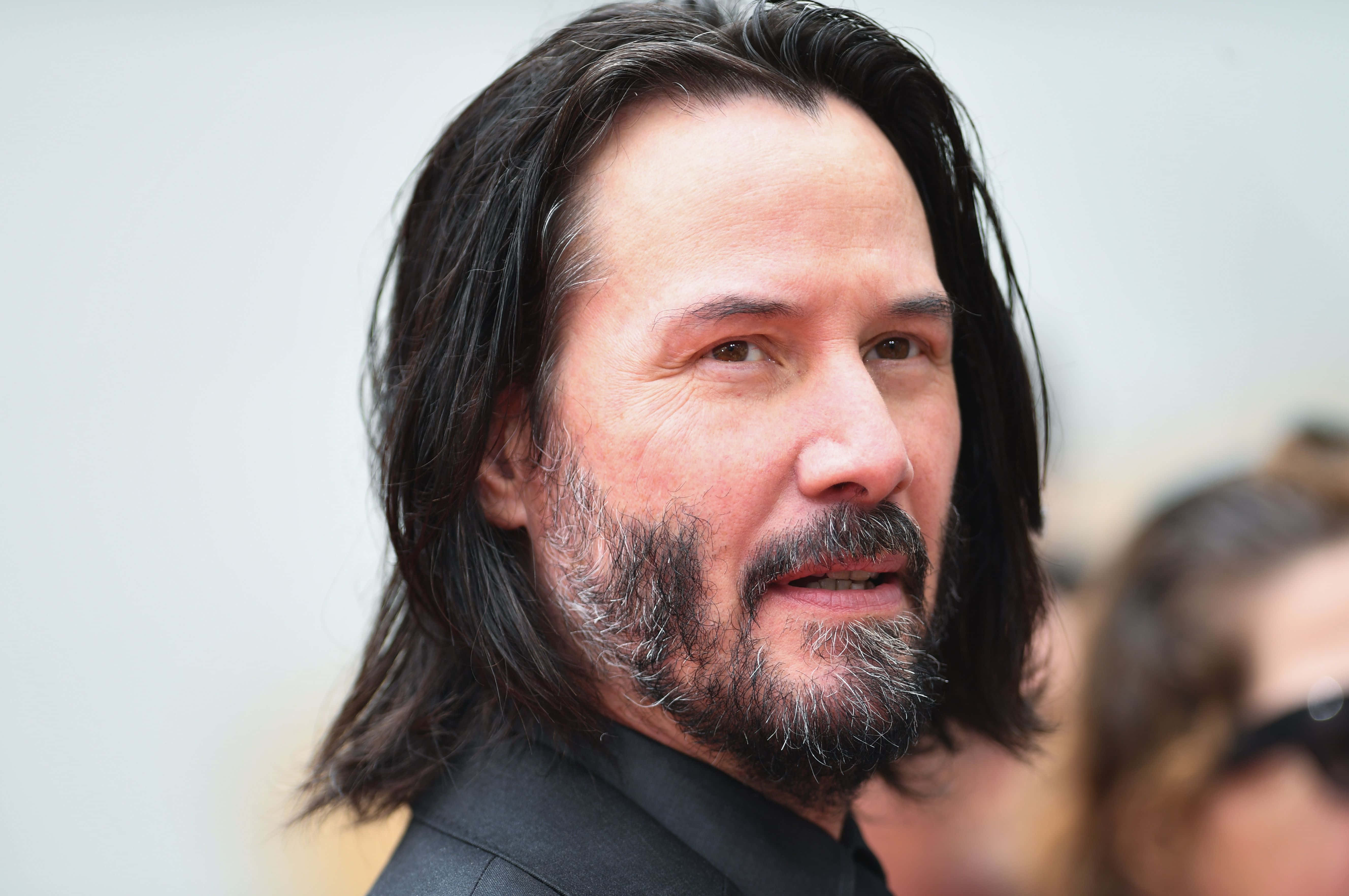 Keanu Reeves 桌布 壁紙 — 奇洛李維斯近距離肖像，長黑髮鬍鬚，身穿黑色西裝，背景模糊。