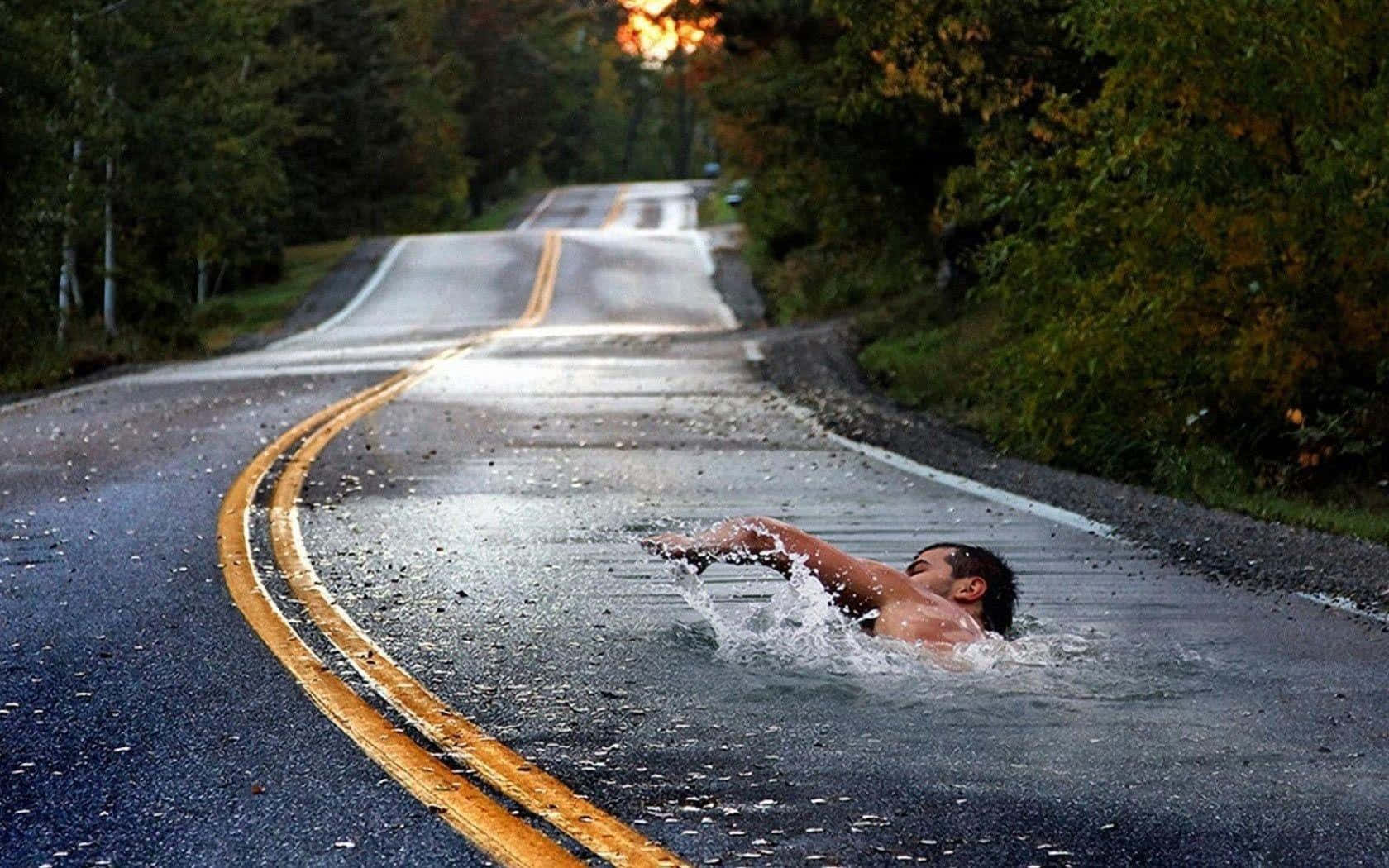 男子在被水淹沒的道路上游泳，周圍是秋日樹木，夕陽照耀