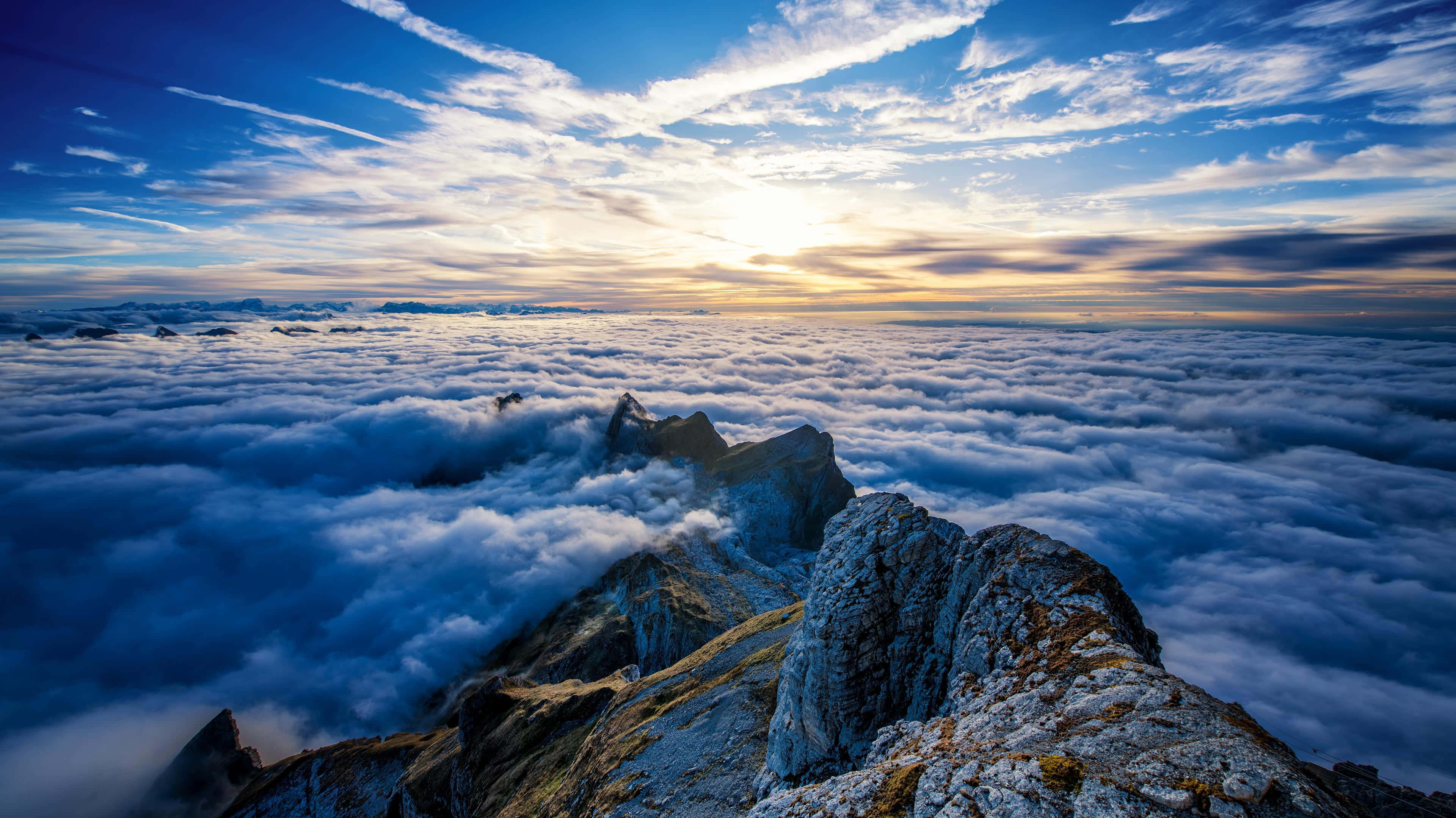 奇蹟般的藍色雲朵背景 壁紙 — 日落沐浴在鋸齒狀山峰之上，雲海之上，令人嘆為觀止的航拍視角。