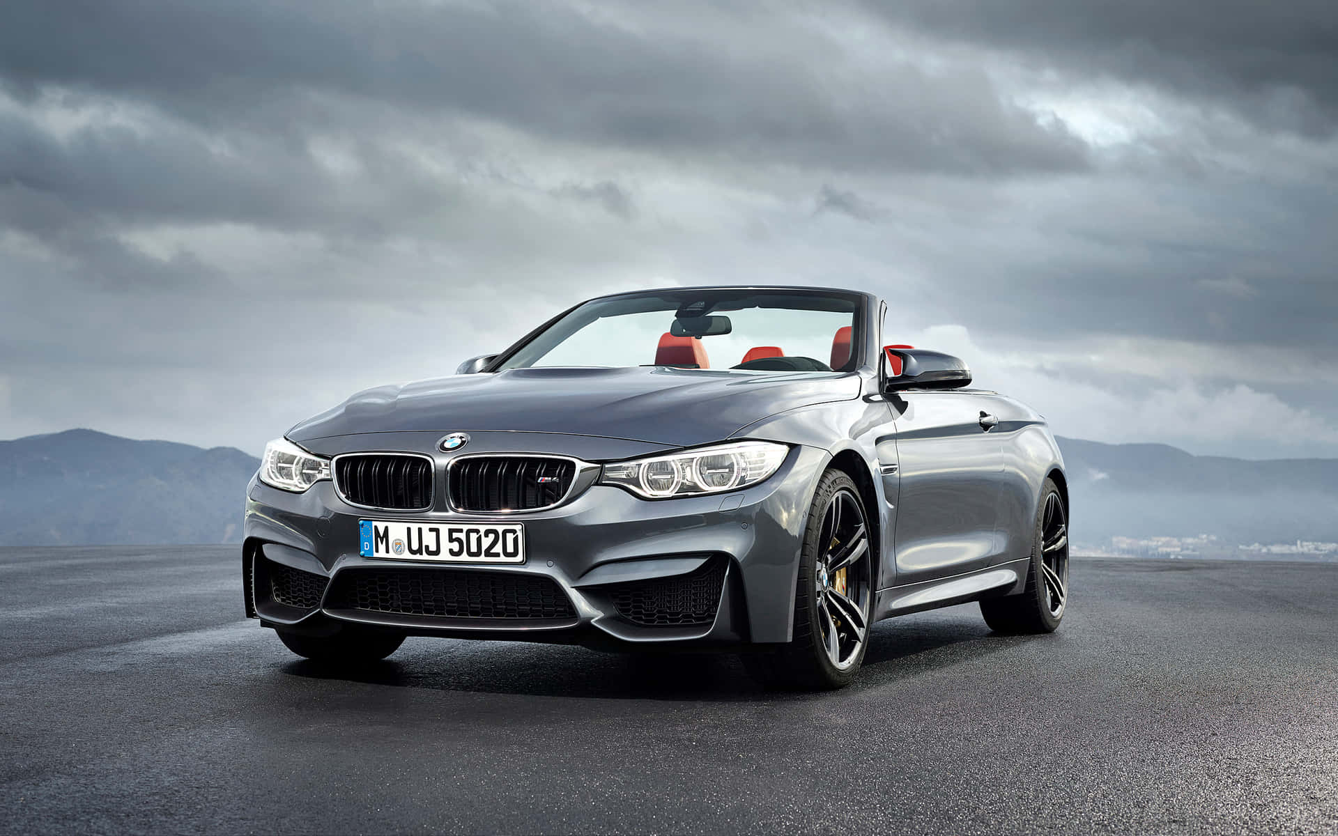 銀色BMW M4開篷車，紅色座椅，濕滑道路，多雲天空。