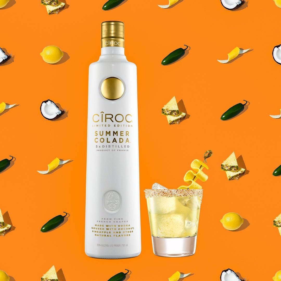 Ciroc Summer Colada伏特加酒瓶和雞尾酒，搭配熱帶水果裝飾，背景為橙色。