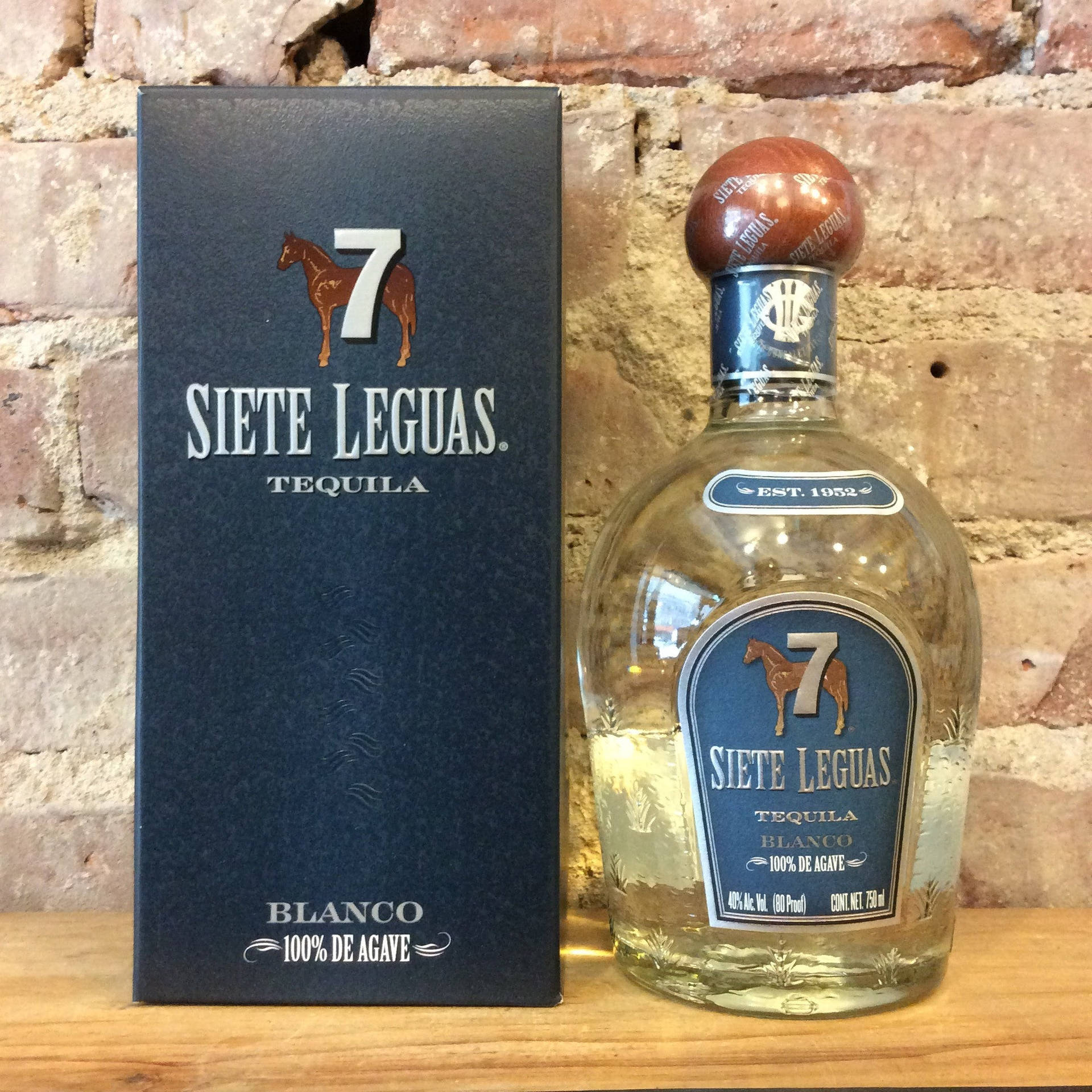 Siete Leguas龍舌蘭酒瓶和盒子在木頭上，背景是磚牆。