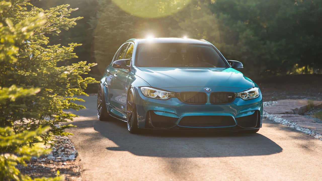 奢華BMW對比光滑質感背景 壁紙 — 一輛青綠色BMW M3跑車在陽光明媚的森林道路上閃耀著金色光芒，並帶有鏡頭光暈。