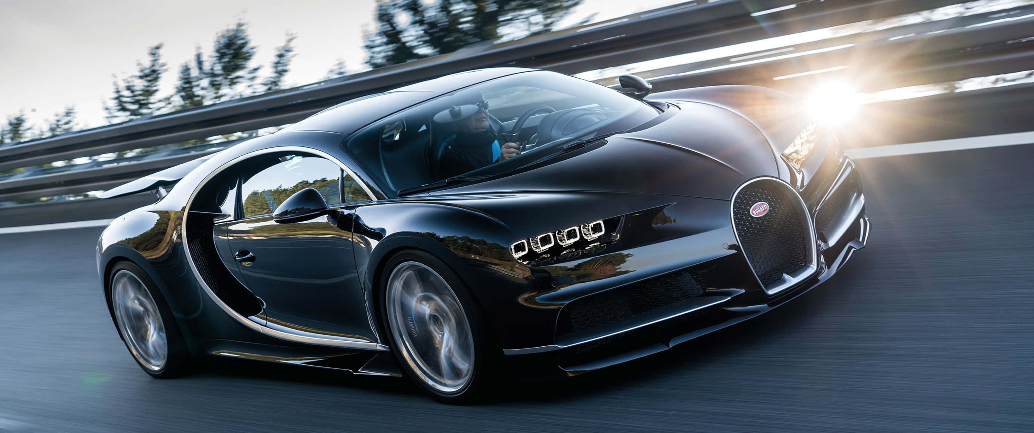 奢華之極——賓利超級賽車 Veyron 壁紙 — 一輛時尚的黑色Bugatti Chiron在蜿蜒的道路上行駛，背景有樹木和明亮的陽光。