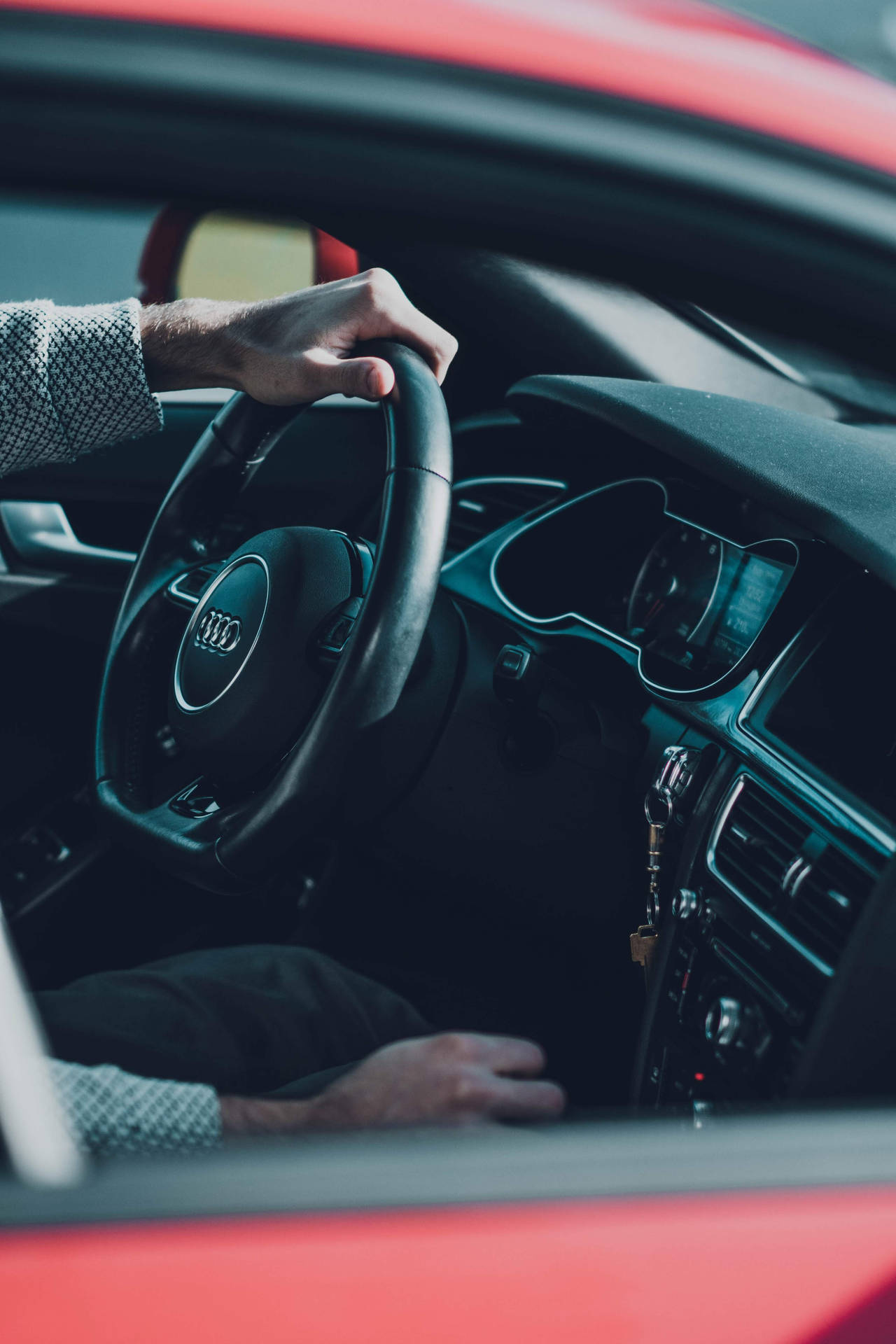 特寫一隻手放在紅色 Audi 汽車的軚盤上，車匙插入點火開關。
