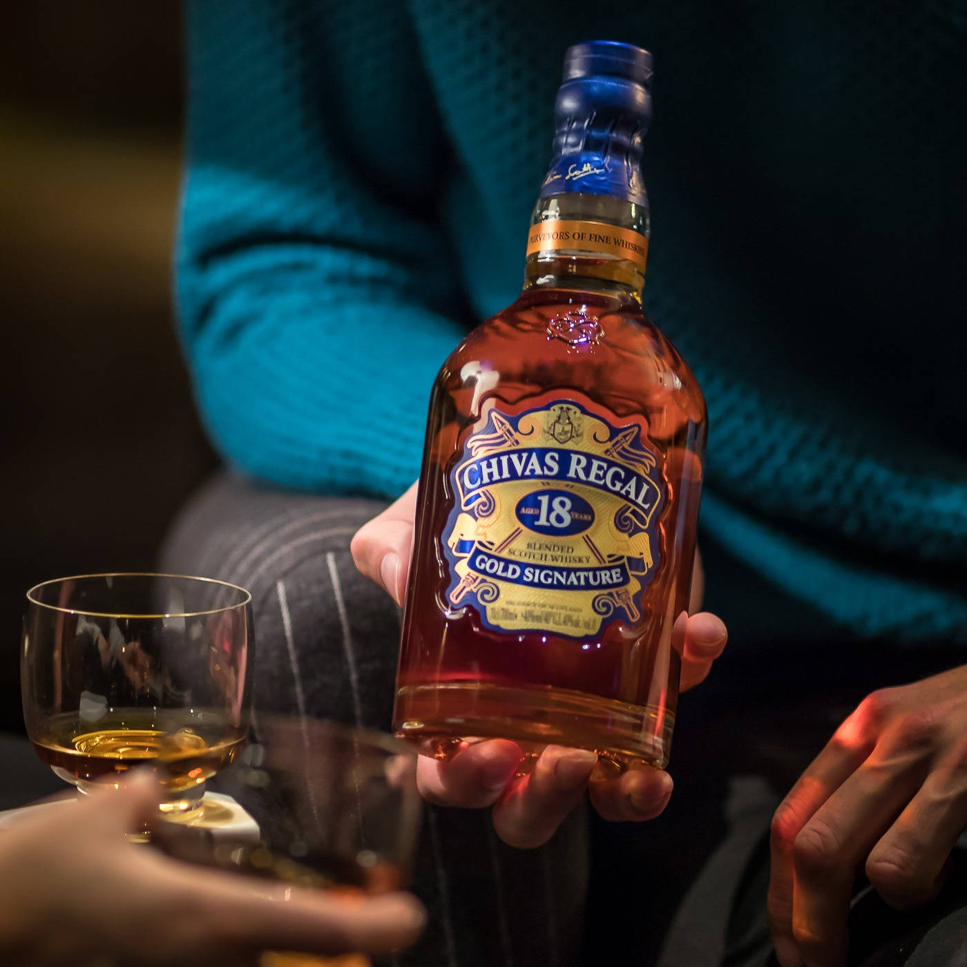 人拿著Chivas Regal威士忌酒瓶，旁邊放著一杯威士忌。