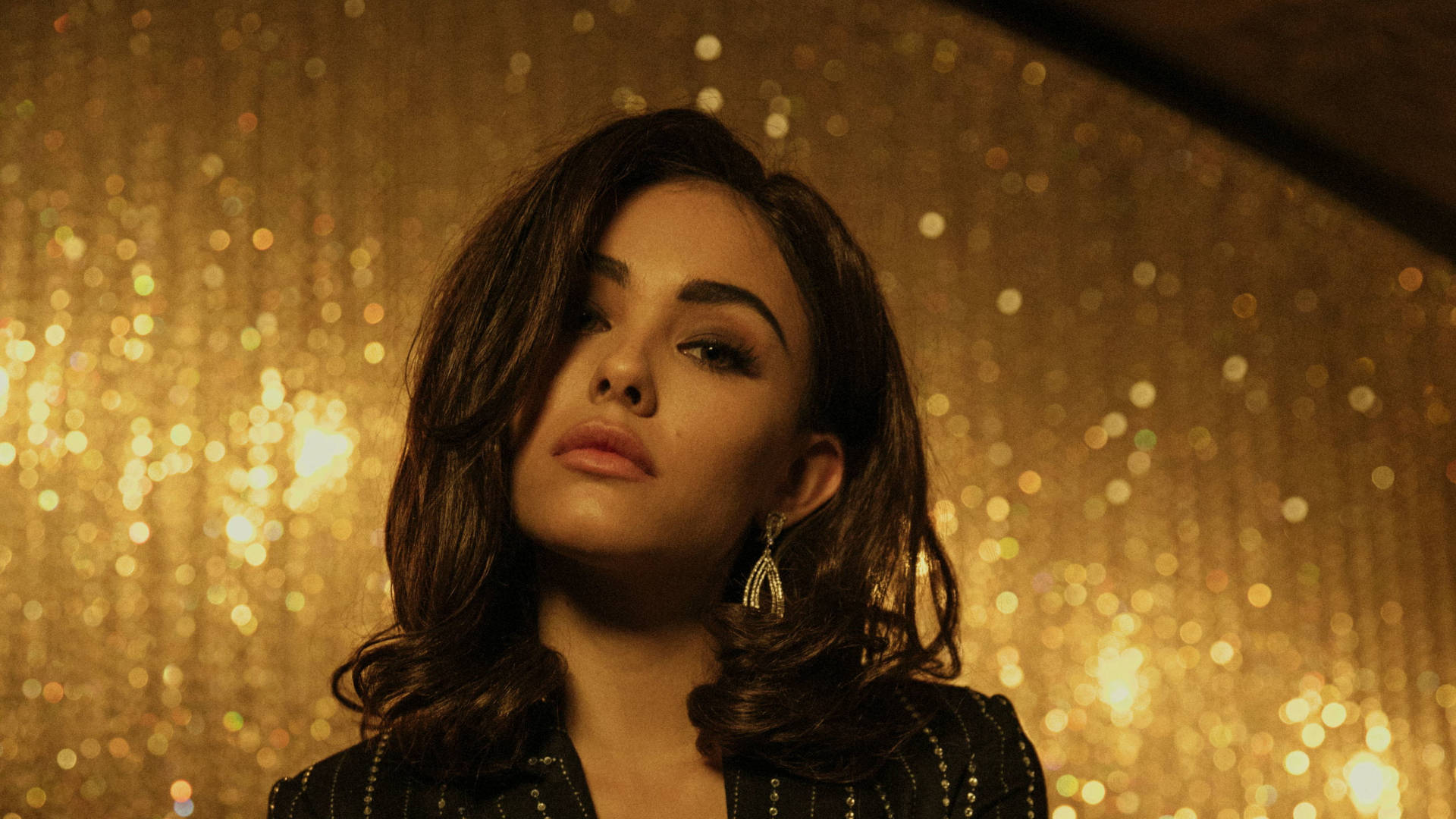 奢華寫真 Madison Beer 壁紙 — 一位深色波浪髮的女性向上凝視，背景是閃爍的金色散景。