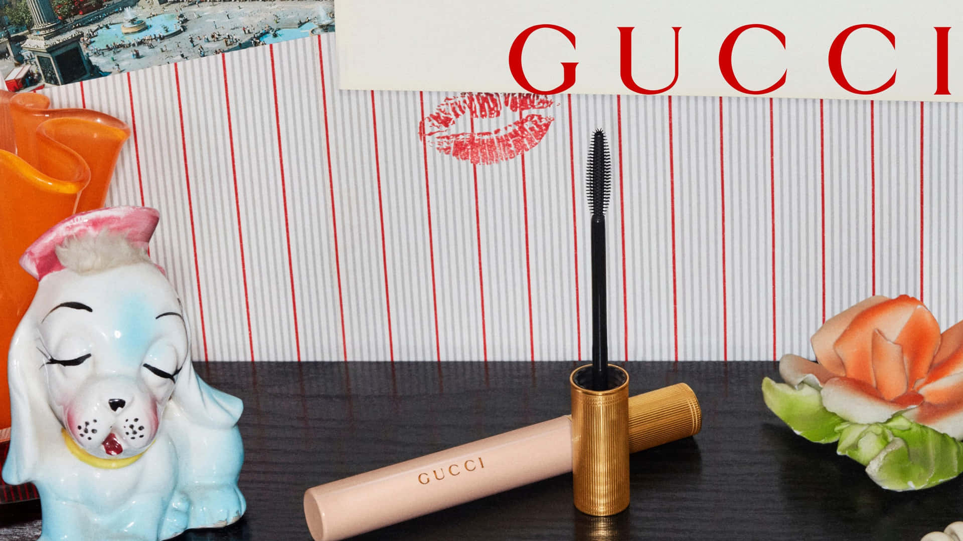 Gucci睫毛膏瓶與復古狗公仔和花卉裝飾在條紋背景上。