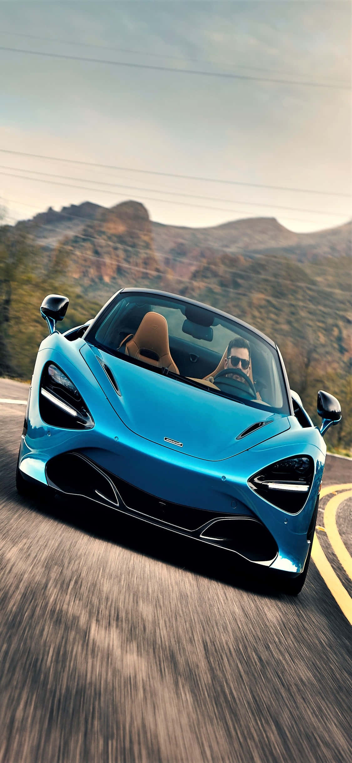 奢華跑車發佈會 影像 壁紙 — 一輛充滿活力的藍色McLaren跑車沿著蜿蜒的山路疾馳，司機戴著太陽眼鏡。