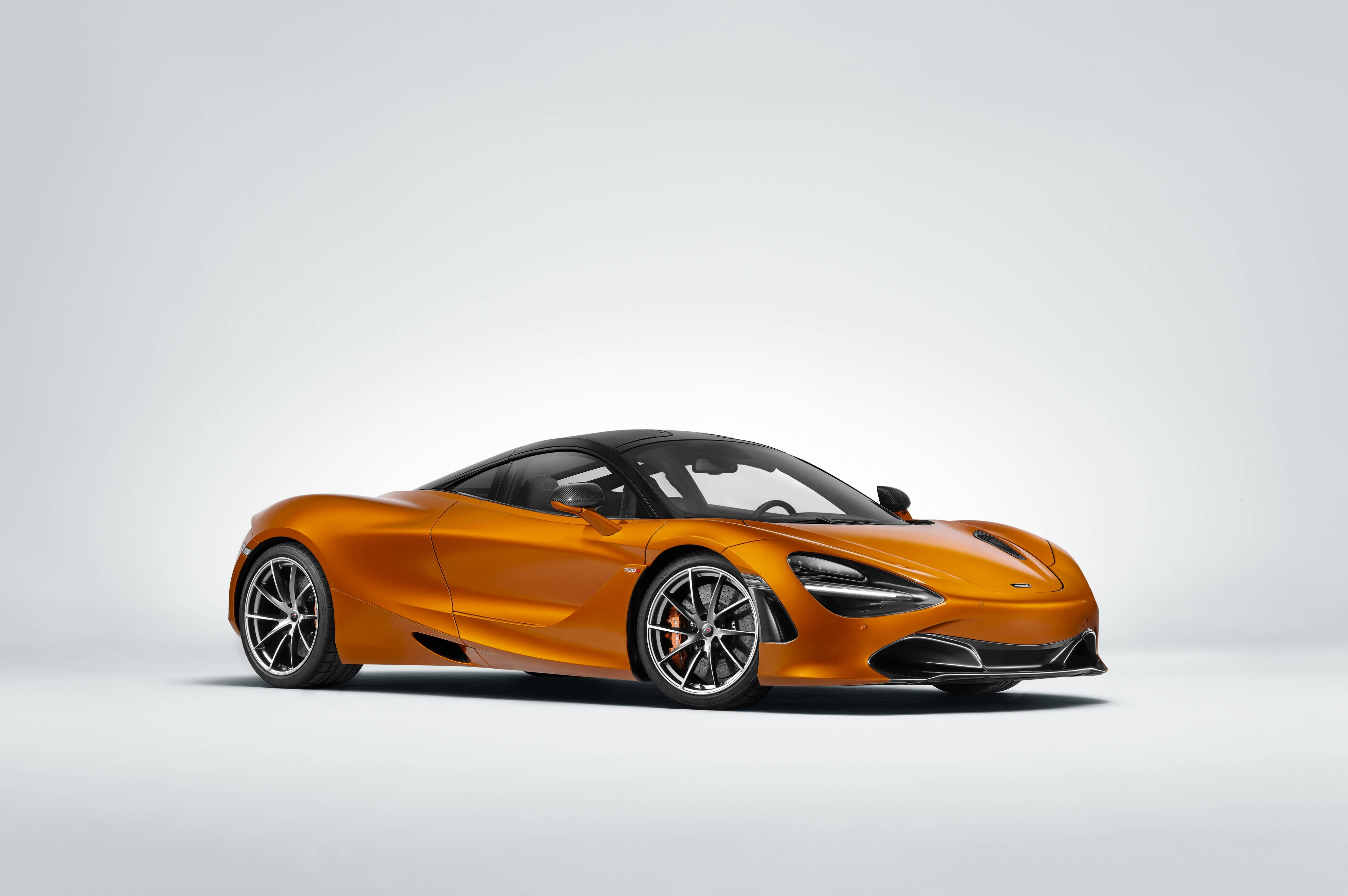 奢華橙色麥拉倫720S 4K 壁紙 — 一輛時尚的橙色McLaren跑車，帶有黑色飾邊和銀色輪圈，擺放在極簡的白色工作室背景前。