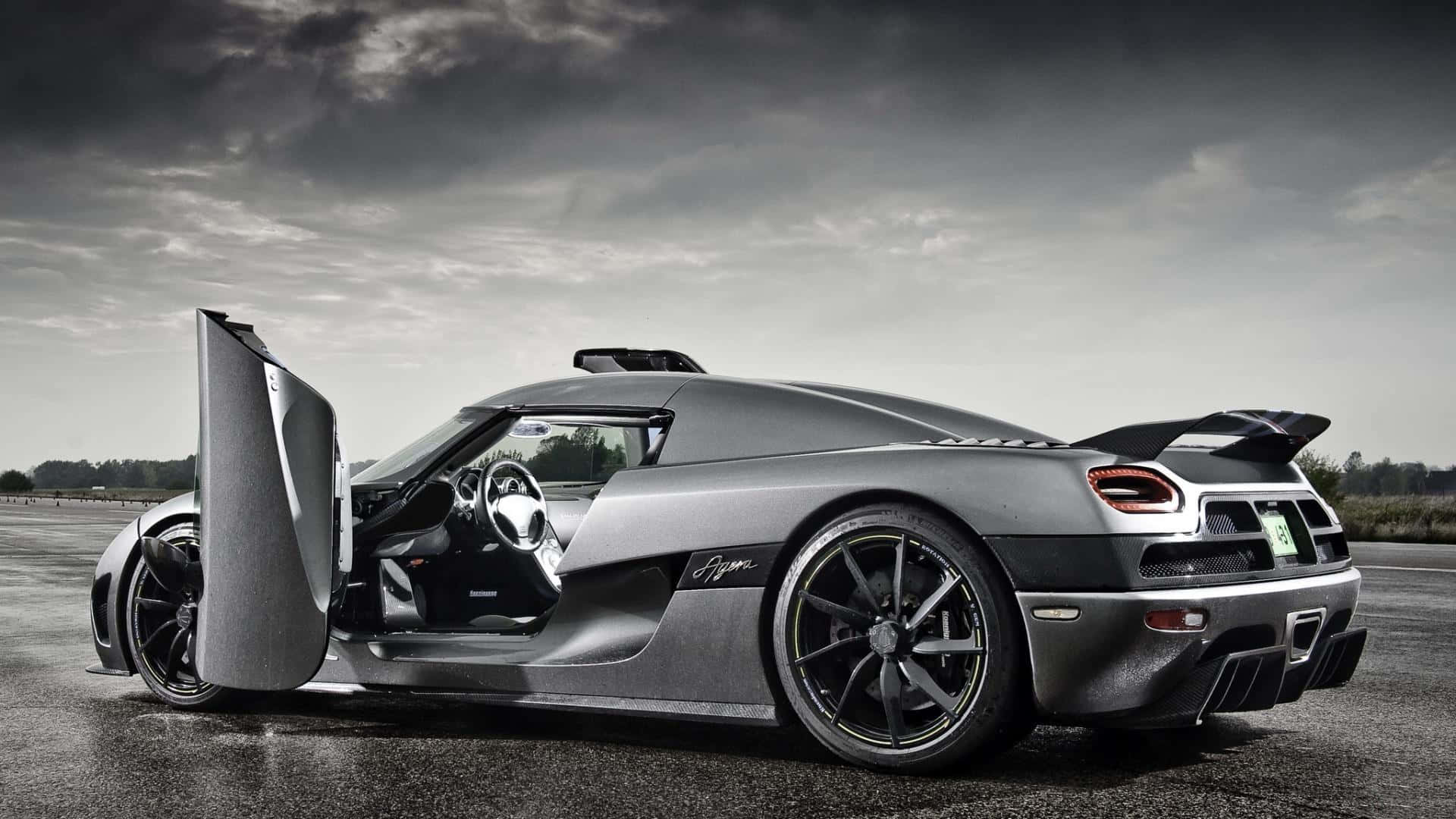 銀色Koenigsegg Agera跑車，鷗翼門打開，在暴風雨天空下的濕滑賽道上。