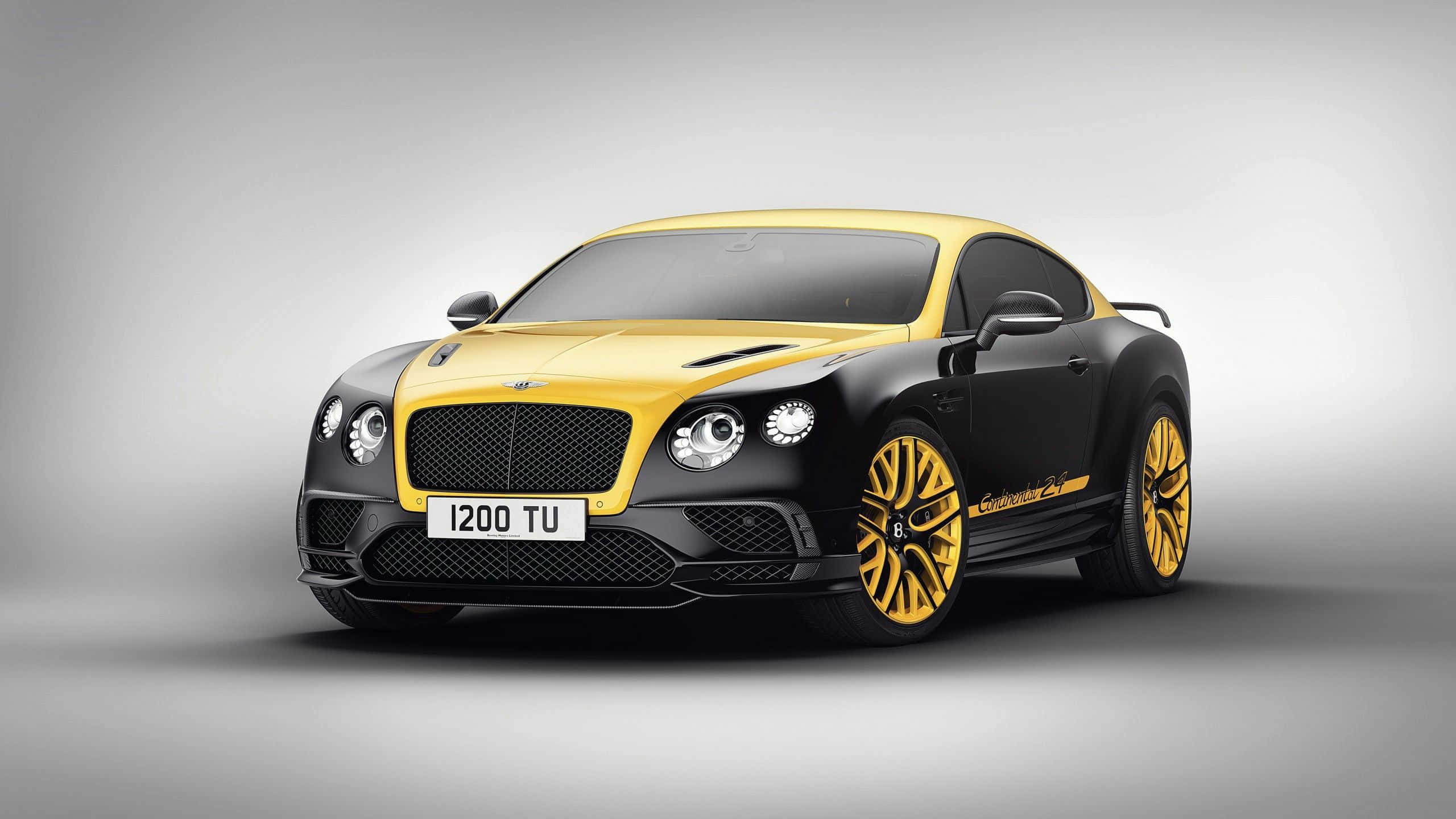 奢華獨特的賓利汽車 壁紙 — 一輛時尚的黑色和黃色 Bentley Continental Supersports 雙門跑車，配備金色輪圈，在灰色中性工作室背景前展示。