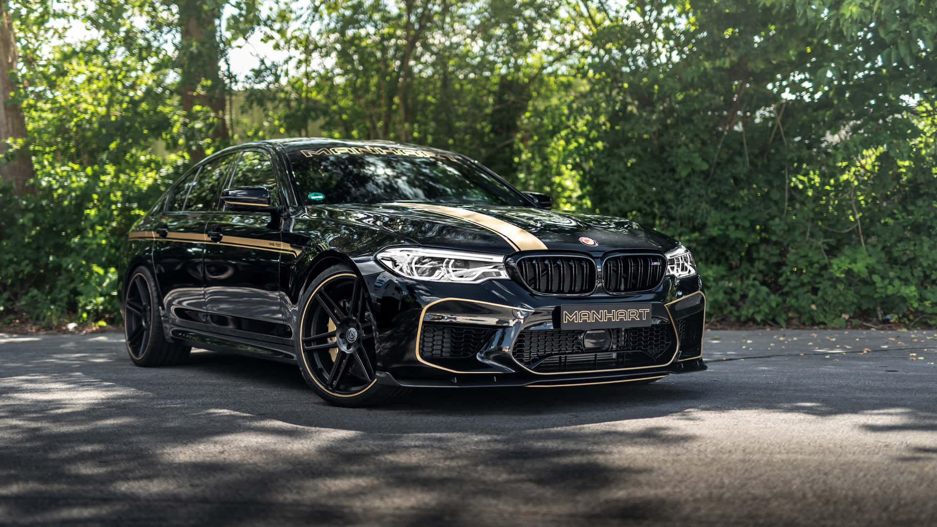 陽光明媚的日子裡，黑色Manhart BMW M5金色飾邊停在樹下。