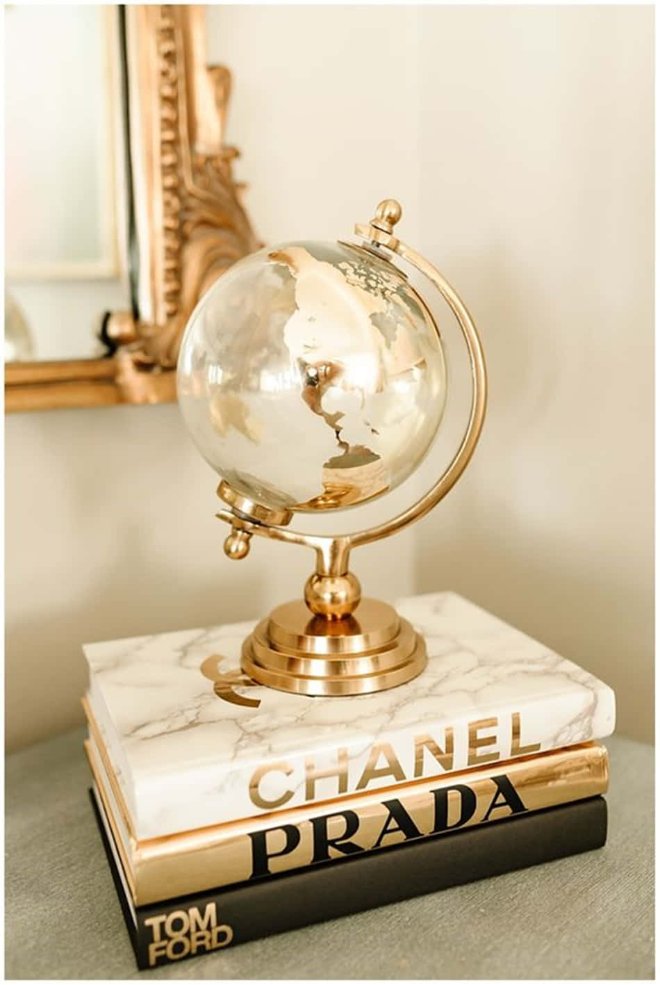 金色地球儀放在 Chanel Prada Tom Ford 書籍堆上，時尚室內環境