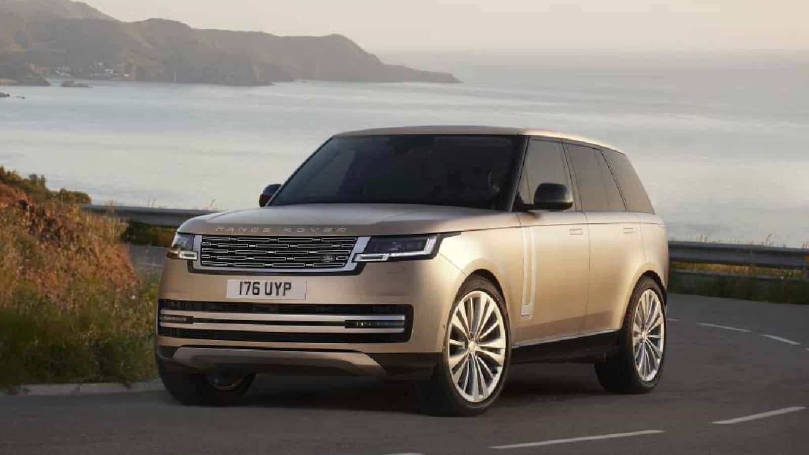 奢華與全地形駕馭：路虎Range Rover 壁紙 — 一輛金色Range Rover SUV在黃金時段沿著海岸道路行駛，背景是山丘和海洋。