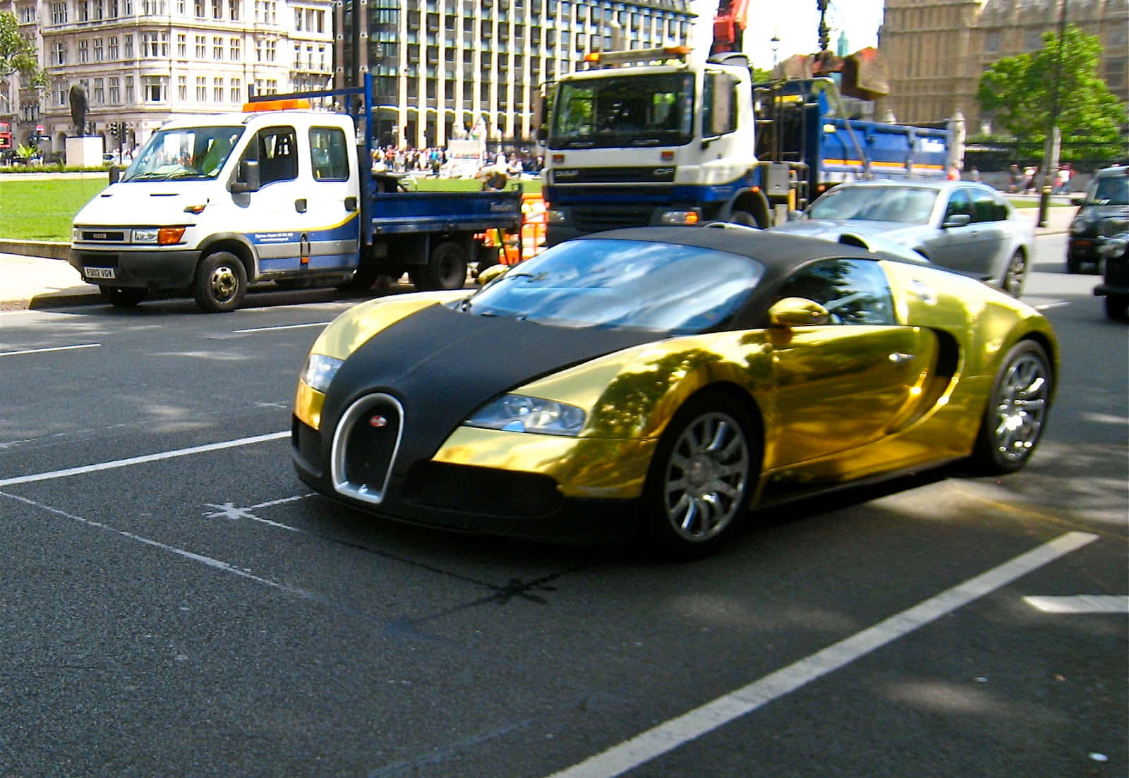 金色和黑色Bugatti Veyron在街道上行駛，有貨車和建築物。