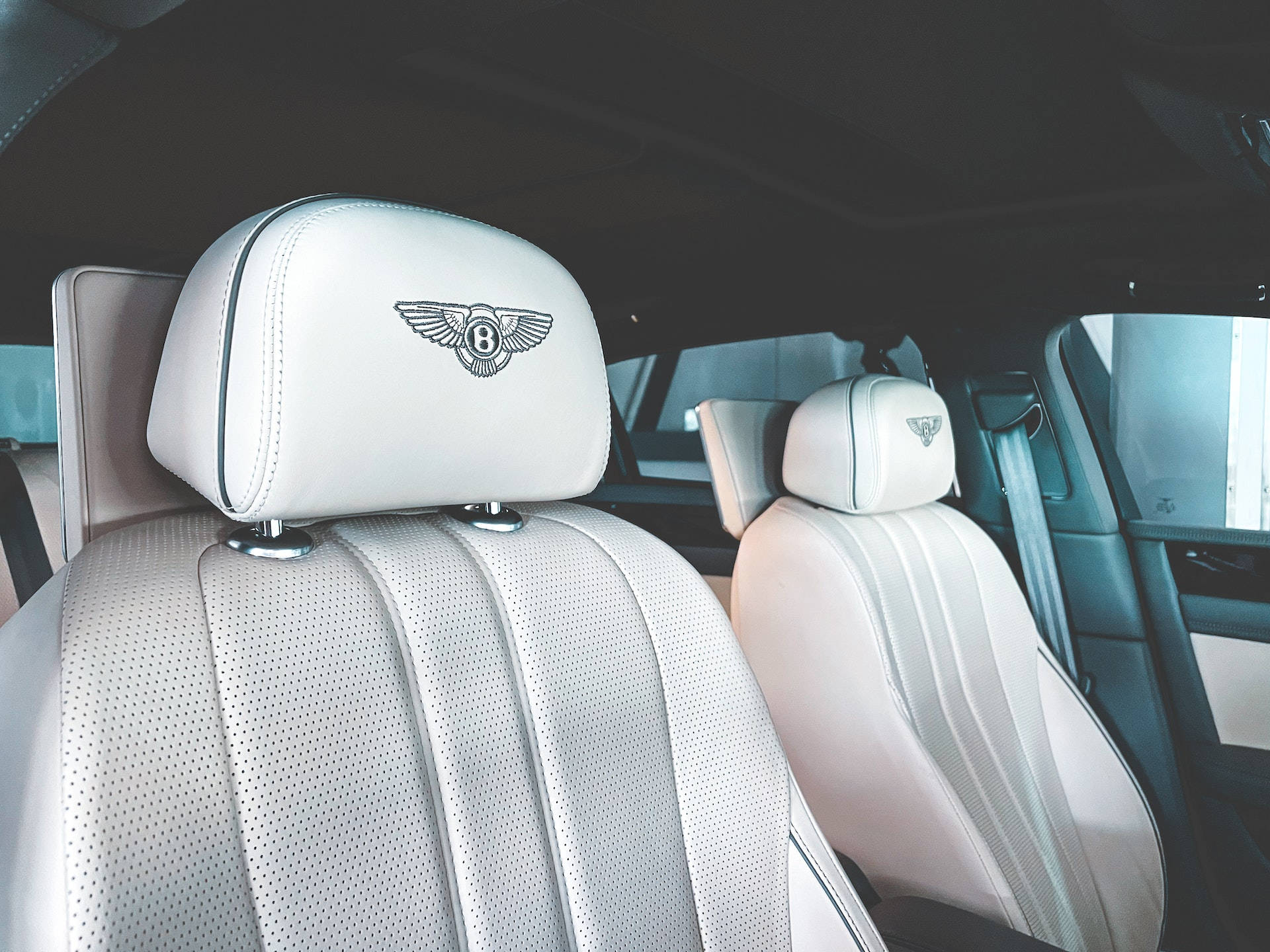 白色皮革 Bentley 汽車座椅，頭枕上帶有翼形 B 標誌。
