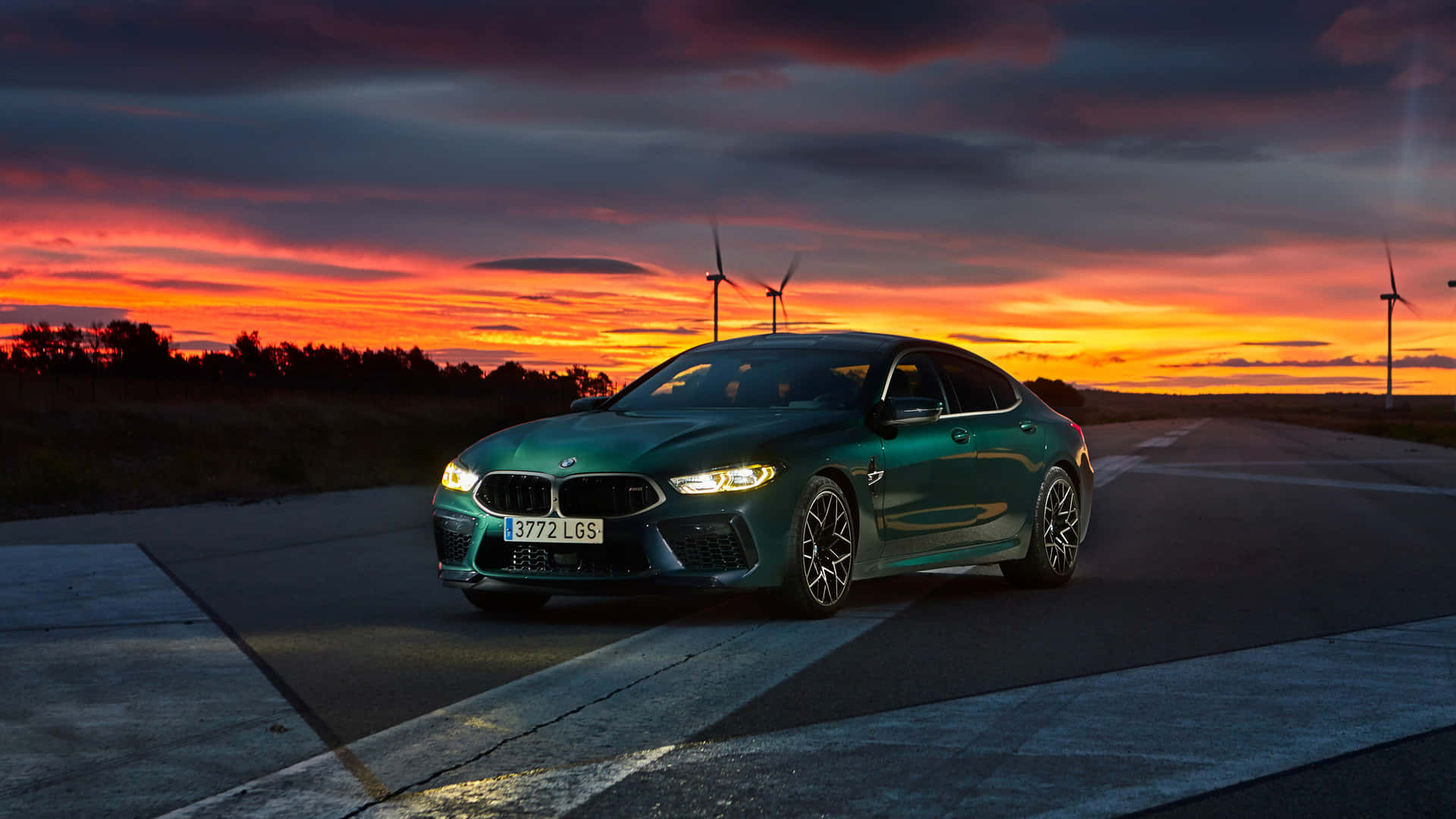 綠色BMW M8 Coupe在日落時停在路上，背景有風力渦輪機。