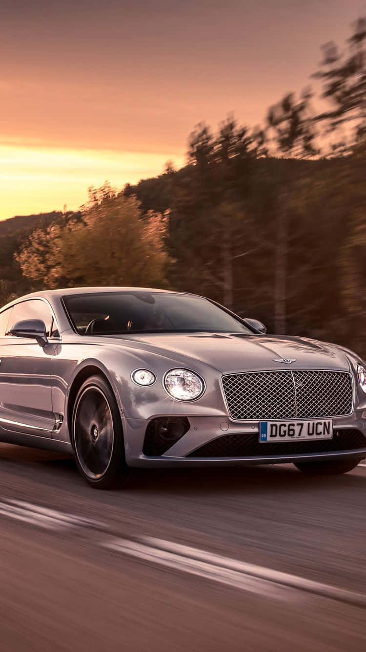 銀色賓利 Continental GT 在日落時分在道路上疾馳，背景有模糊的樹木。
