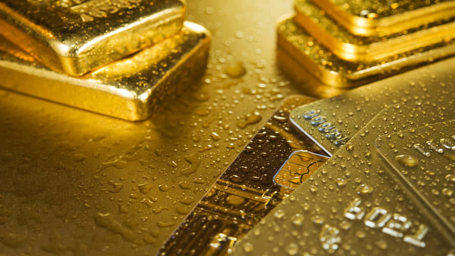 奢華閃亮金背景 壁紙 — 閃閃發光的金條和信用卡在反光的金色表面上閃爍著水滴。