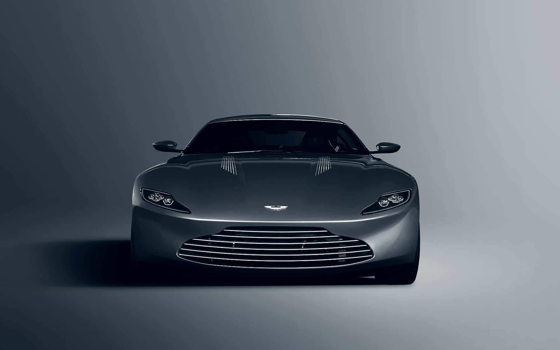 奢華阿斯頓·馬丁概念車 壁紙 — 一輛時尚的深灰色 Aston Martin 跑車在極簡風格的工作室中正面朝前，配有柔和的漸變燈光。