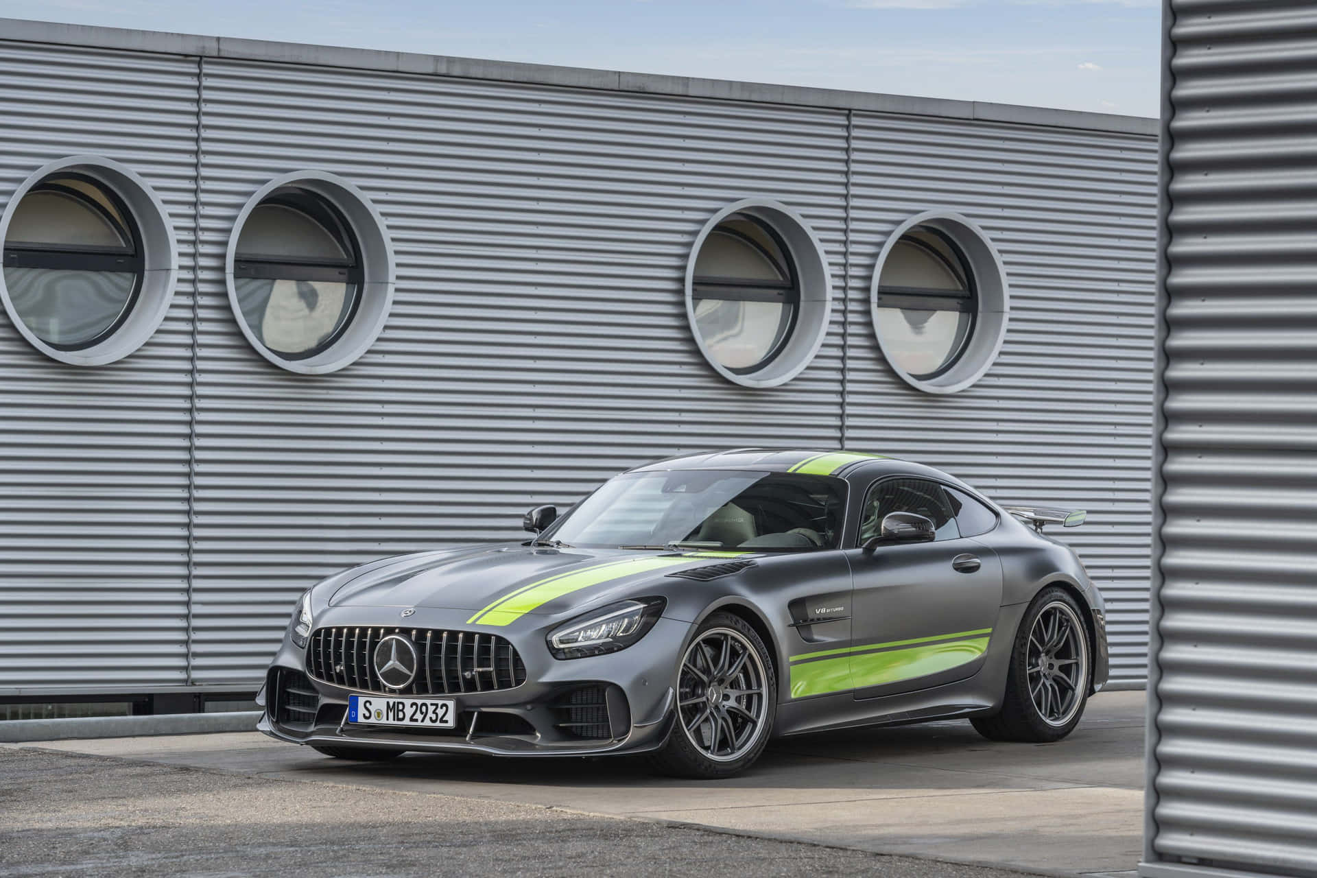 灰色Mercedes-AMG GT跑車，帶有綠色點綴，停在工業建築附近。