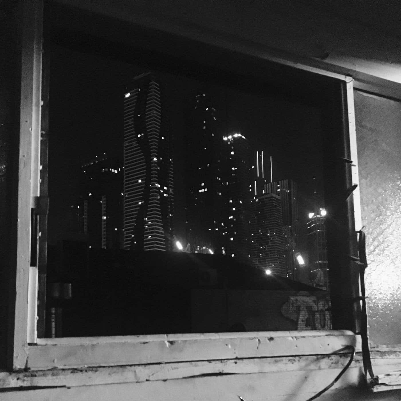 透過帶有塗鴉的破舊窗戶觀賞城市摩天大樓的夜景。