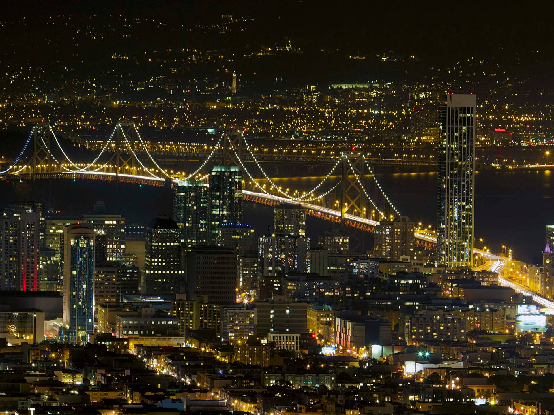 城市夜景，有燈光璀璨的吊橋橫跨水面和發光的摩天大樓。