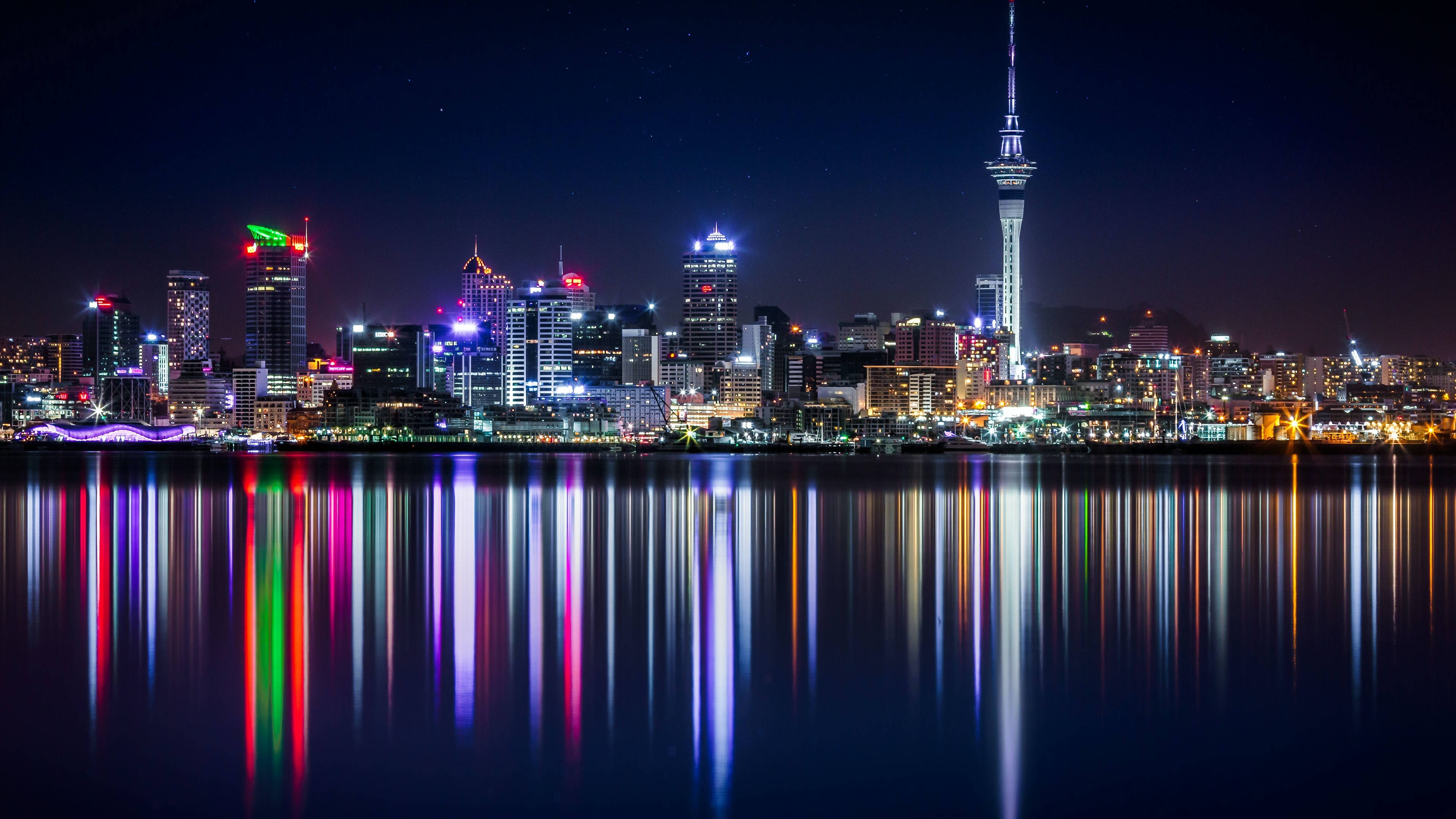 奧克蘭市海濱高樓夜景 壁紙 — 在星空下，平靜的水面完美映照出璀璨的摩天大樓燈光，構成迷人的夜景。