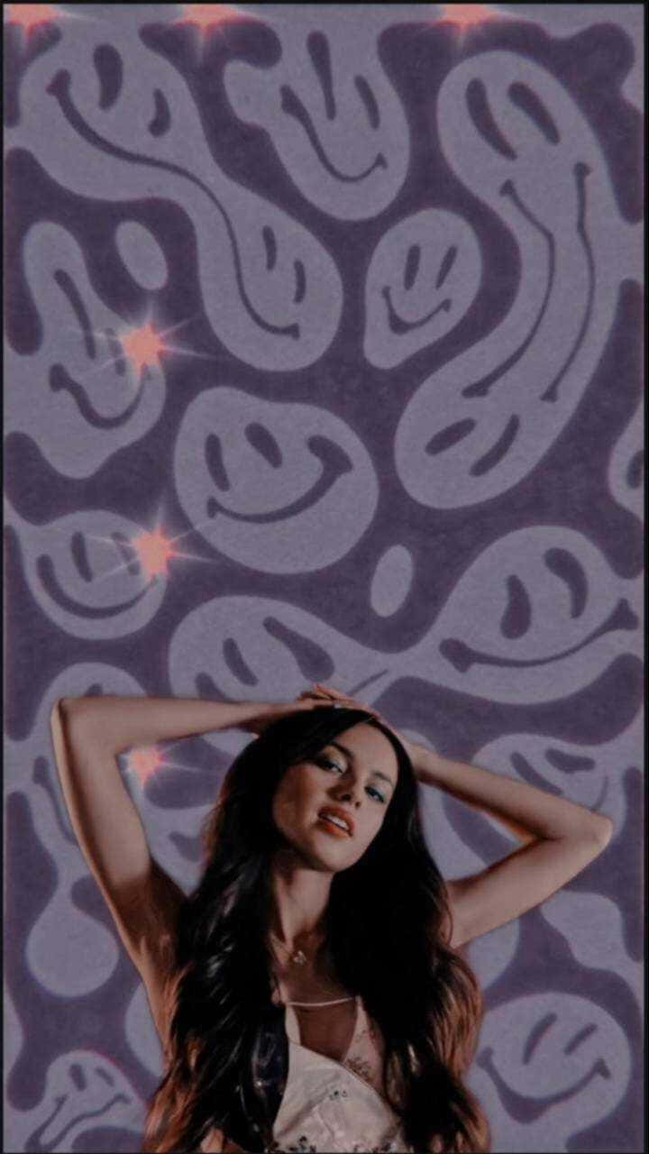 女性在紫色笑臉牆紙前將手放在頭髮上擺姿勢。