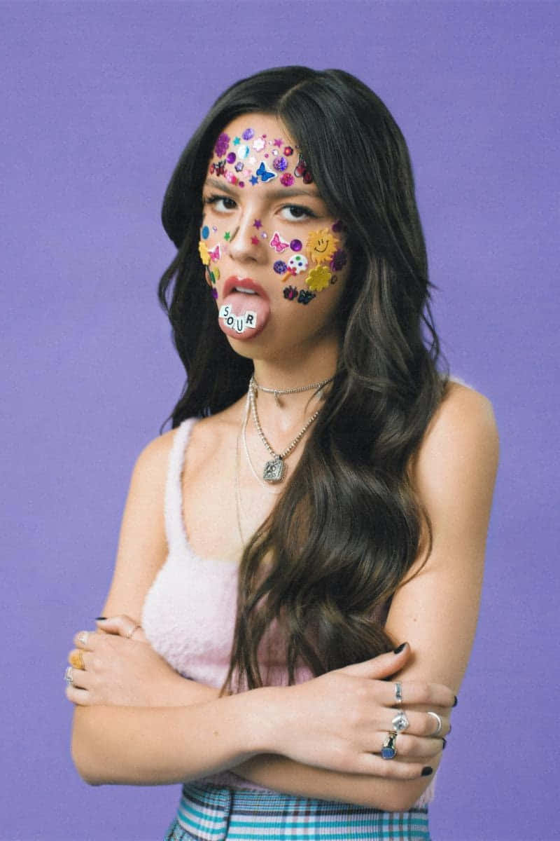 年輕女性臉上貼著貼紙並伸出舌頭，背景為紫色