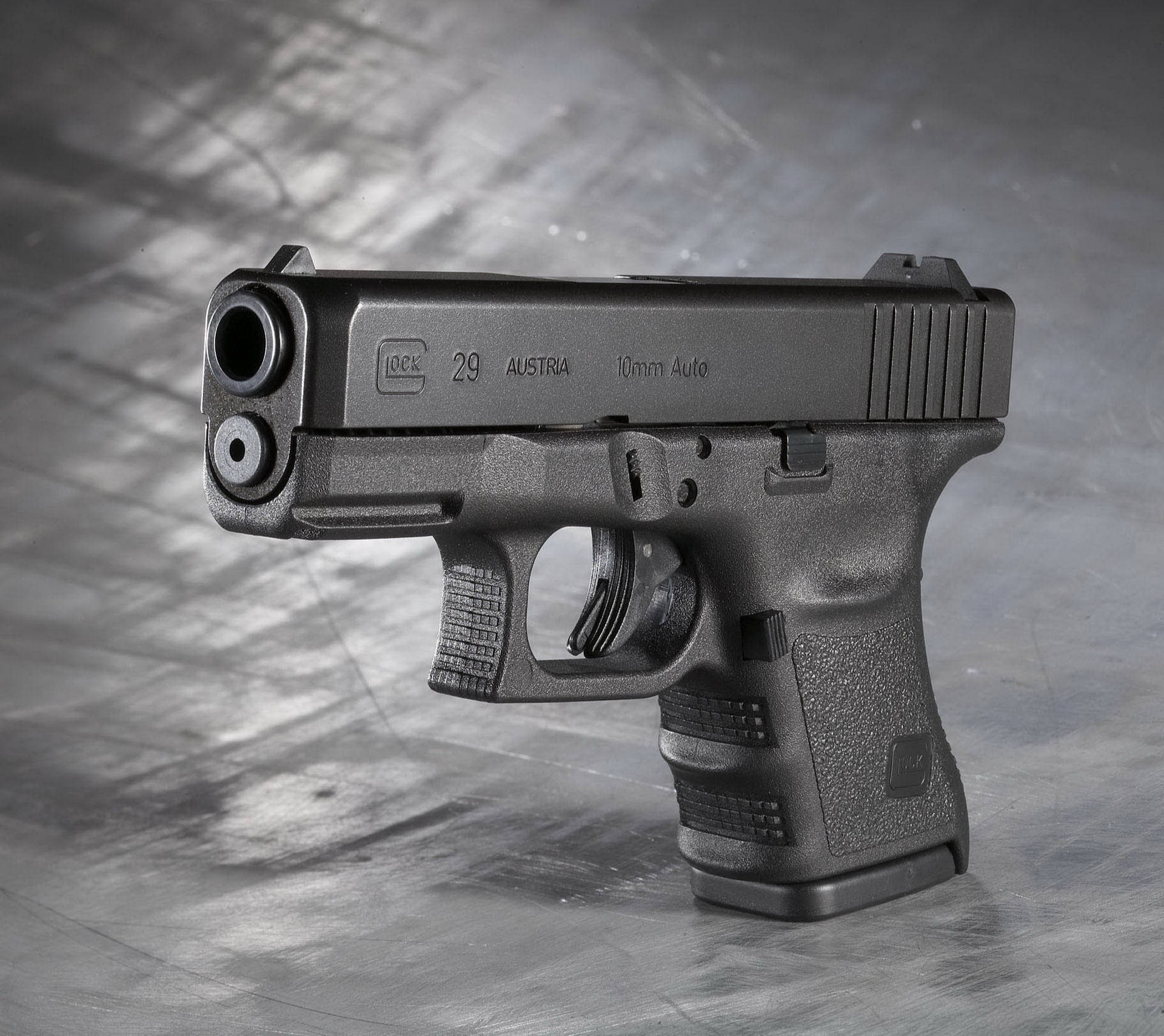 奧地利黑色格洛克29 壁紙 — 一把時尚的黑色 Glock 29 手槍放在有紋理的金屬表面上，在戲劇性的工作室燈光下。