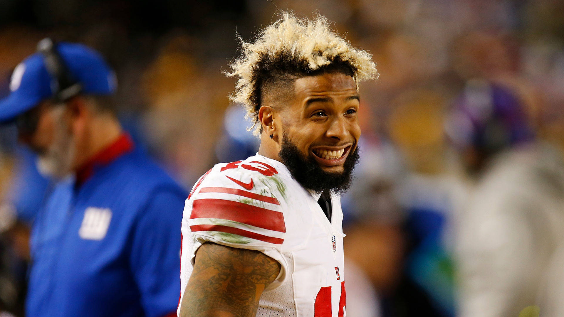 NFL美式足球運動員微笑，漂白頭髮和鬍鬚，在夜間球場。