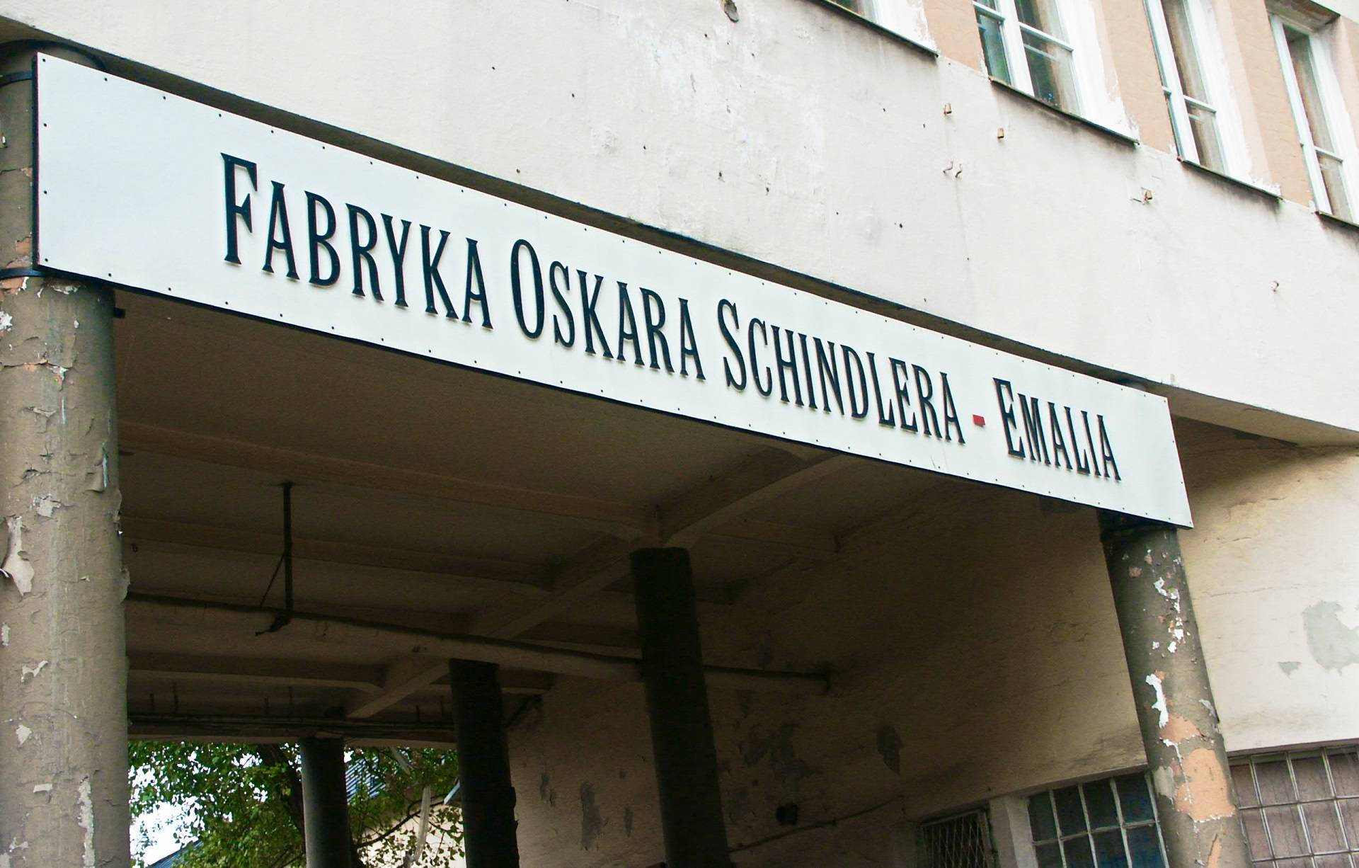 奧斯卡·辛德勒工廠 波蘭 壁紙 — 一塊風化的招牌，上面寫著 Fabryka Oskara Schindlera Emalia，掛在一棟破舊工業建築的入口上方。