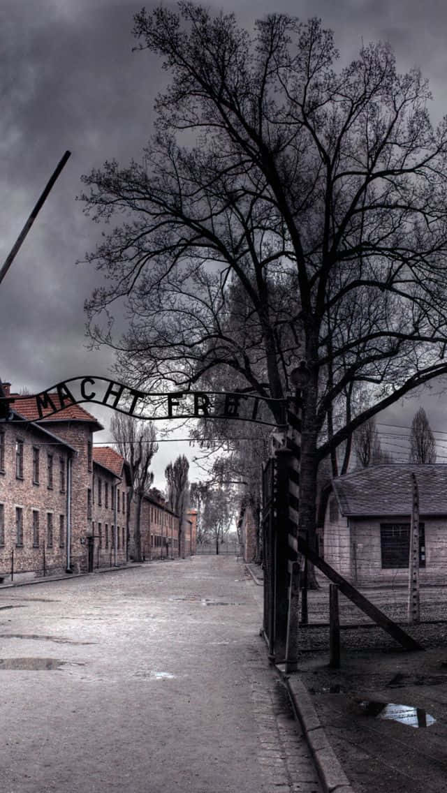 暴風雨天空下，奧斯威辛集中營入口帶有「Arbeit macht frei」標誌。