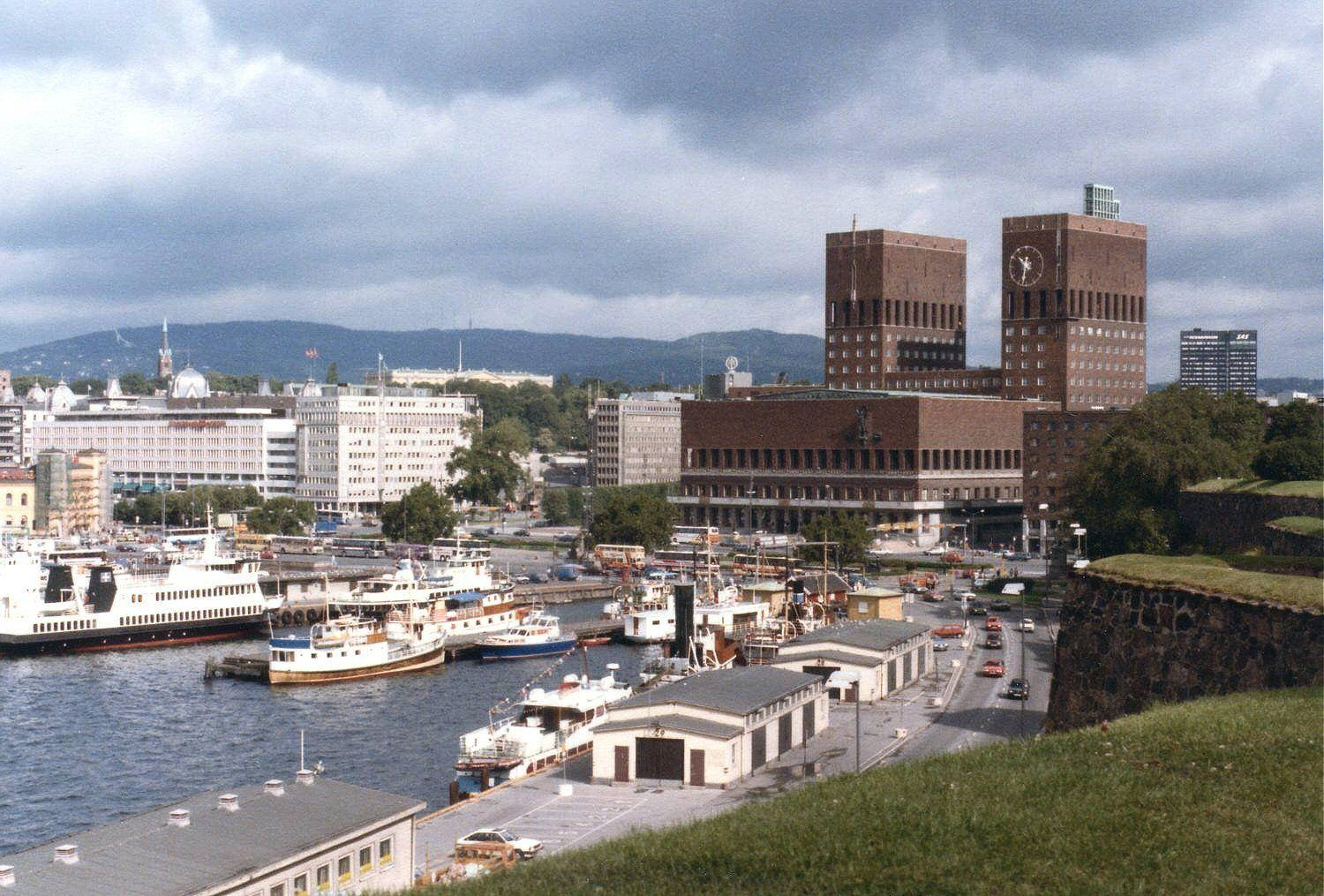 奧斯陸城市河景 壁紙 — 奧斯陸港口的全景，船隻停泊，標誌性的奧斯陸市政廳塔樓在陰雲密佈的天空下聳立。