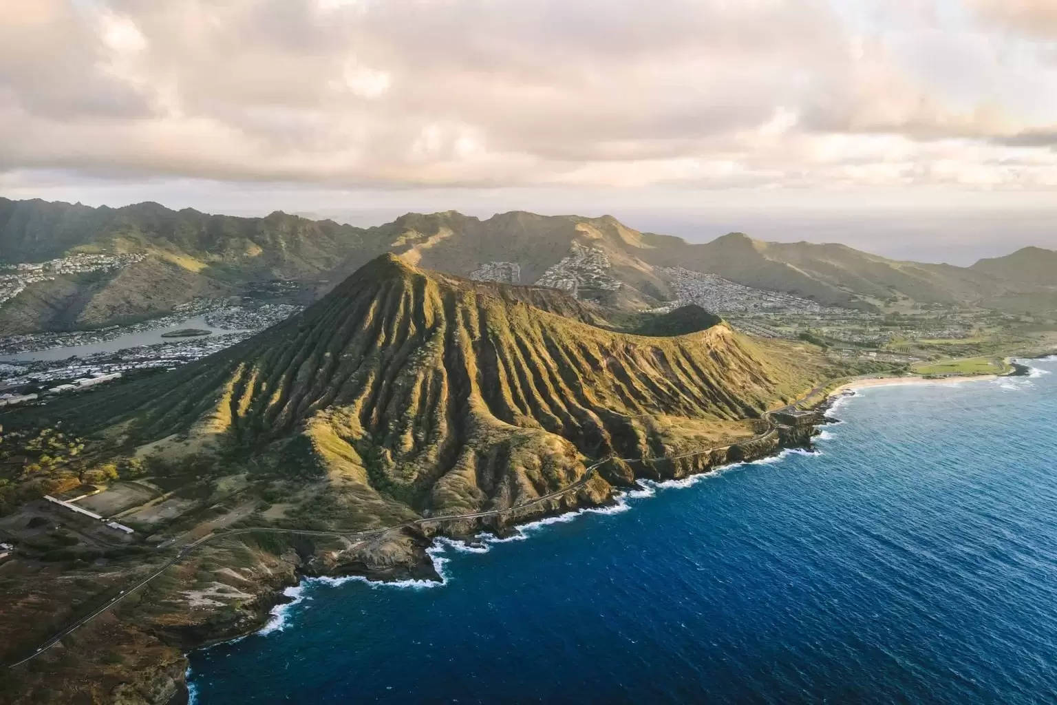 奧胡島火山錐與藍色海洋 壁紙 — 鑽石頭火山口的鳥瞰圖，在金色夕陽光芒中閃耀，旁邊是碧綠的海洋和沿海城鎮。