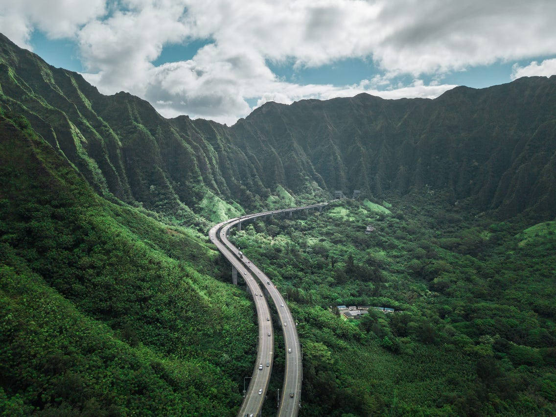 奧胡島長途公路 壁紙 — 一條蜿蜒的高速公路在部分多雲的天空下蜿蜒穿過鬱鬱蔥蔥的綠色山谷。