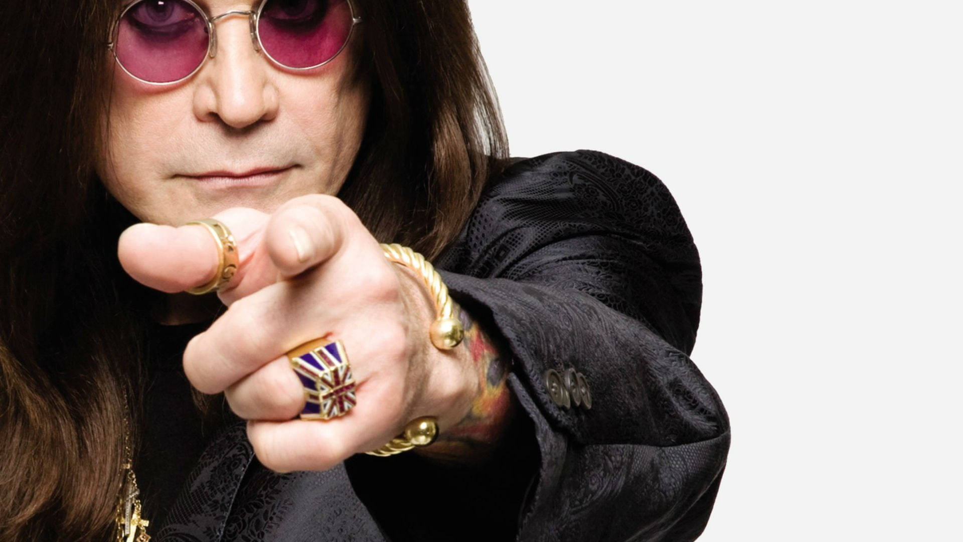 Ozzy Osbourne 戴著粉紅色太陽眼鏡和金色戒指指向觀眾。