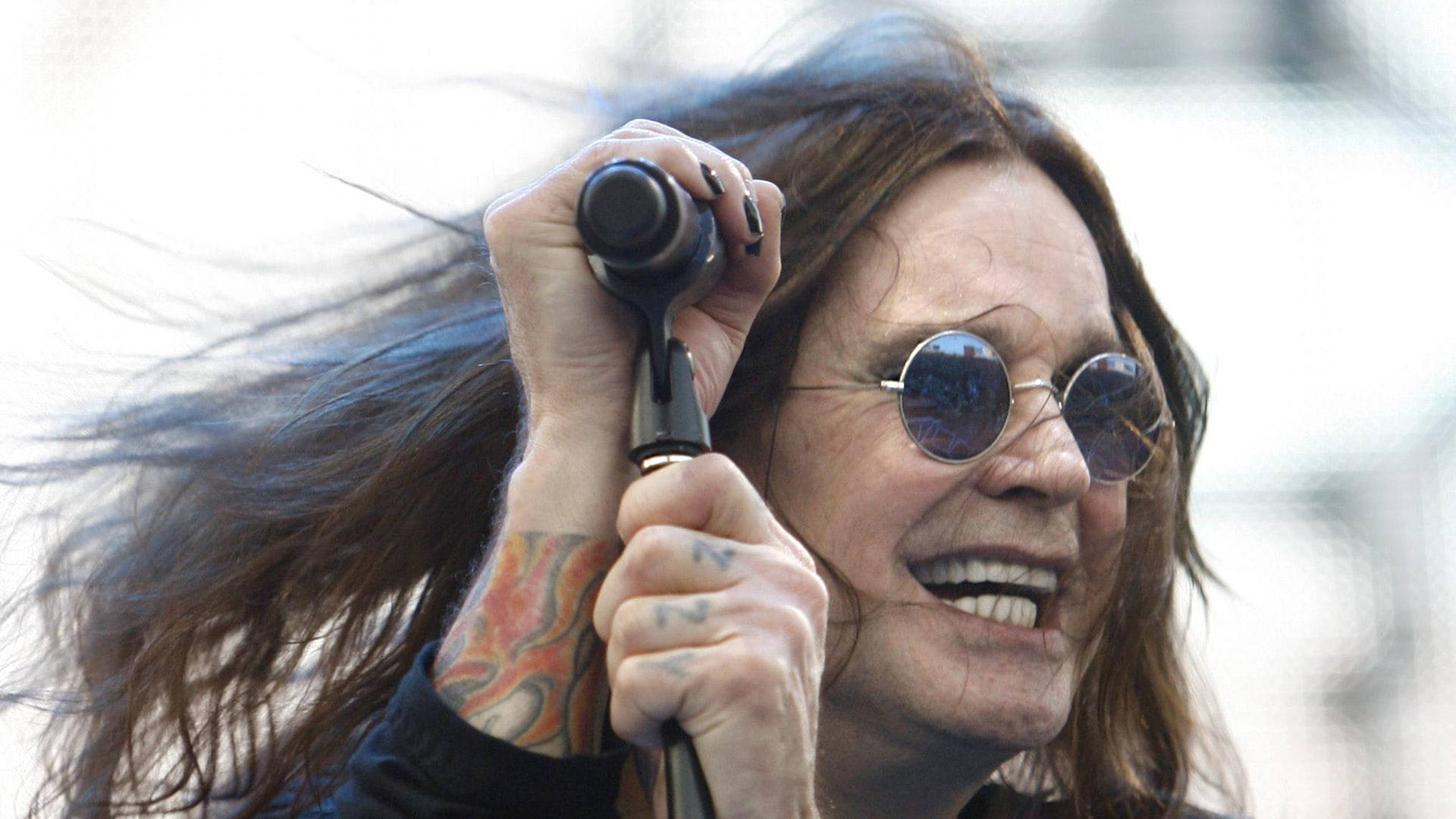 Ozzy Osbourne 對著咪高峰唱歌，風吹動他的頭髮。