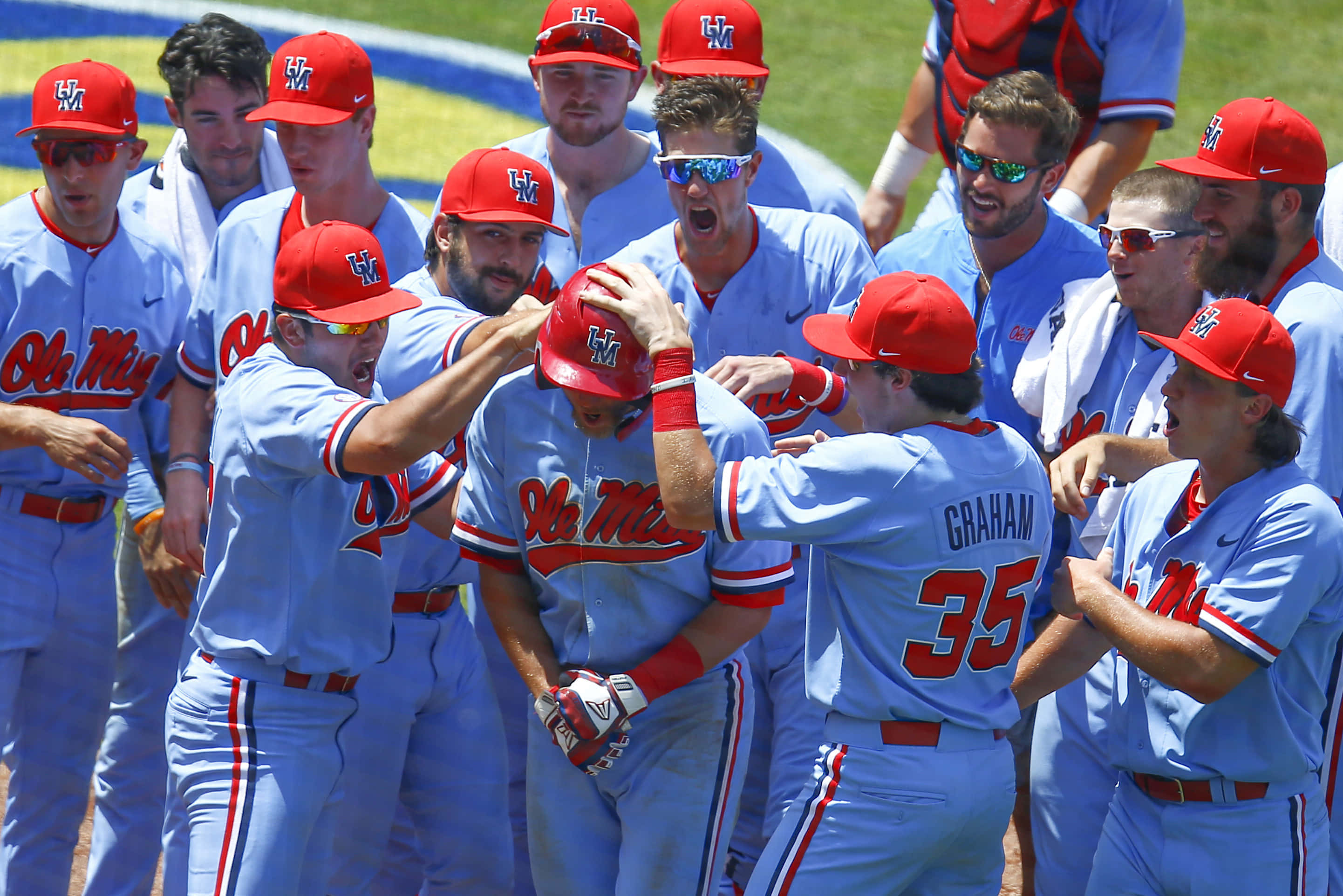 College Baseball 桌布 壁紙 — 奧萊密斯棒球選手身穿淺藍色和紅色制服，在陽光明媚的球場上熱情慶祝。