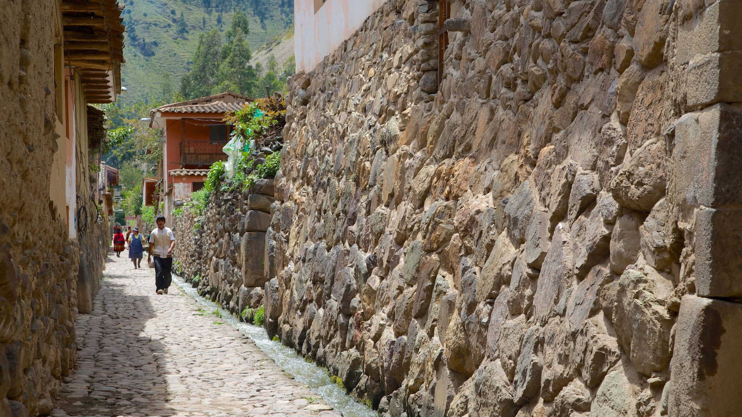 奧蘭塔坦博山谷的印加考古遺跡 壁紙 — 一條狹窄的鵝卵石小巷，位於山村中，兩旁是古老的石牆和色彩繽紛的建築，在明亮的日光下。